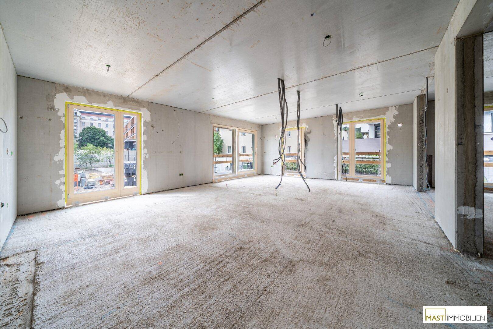Weitläufiger Rohbau-Innenraum mit mehreren Fensteröffnungen und Betonoberflächen.