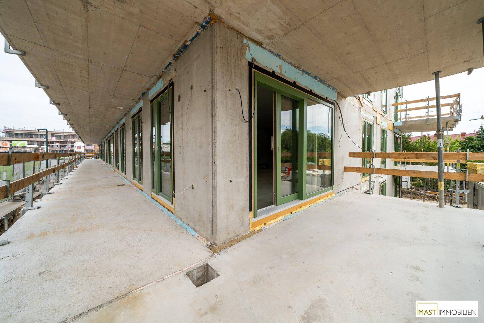 Lange, unfertige Betonterrasse eines Neubaus mit temporären Holzgeländern.