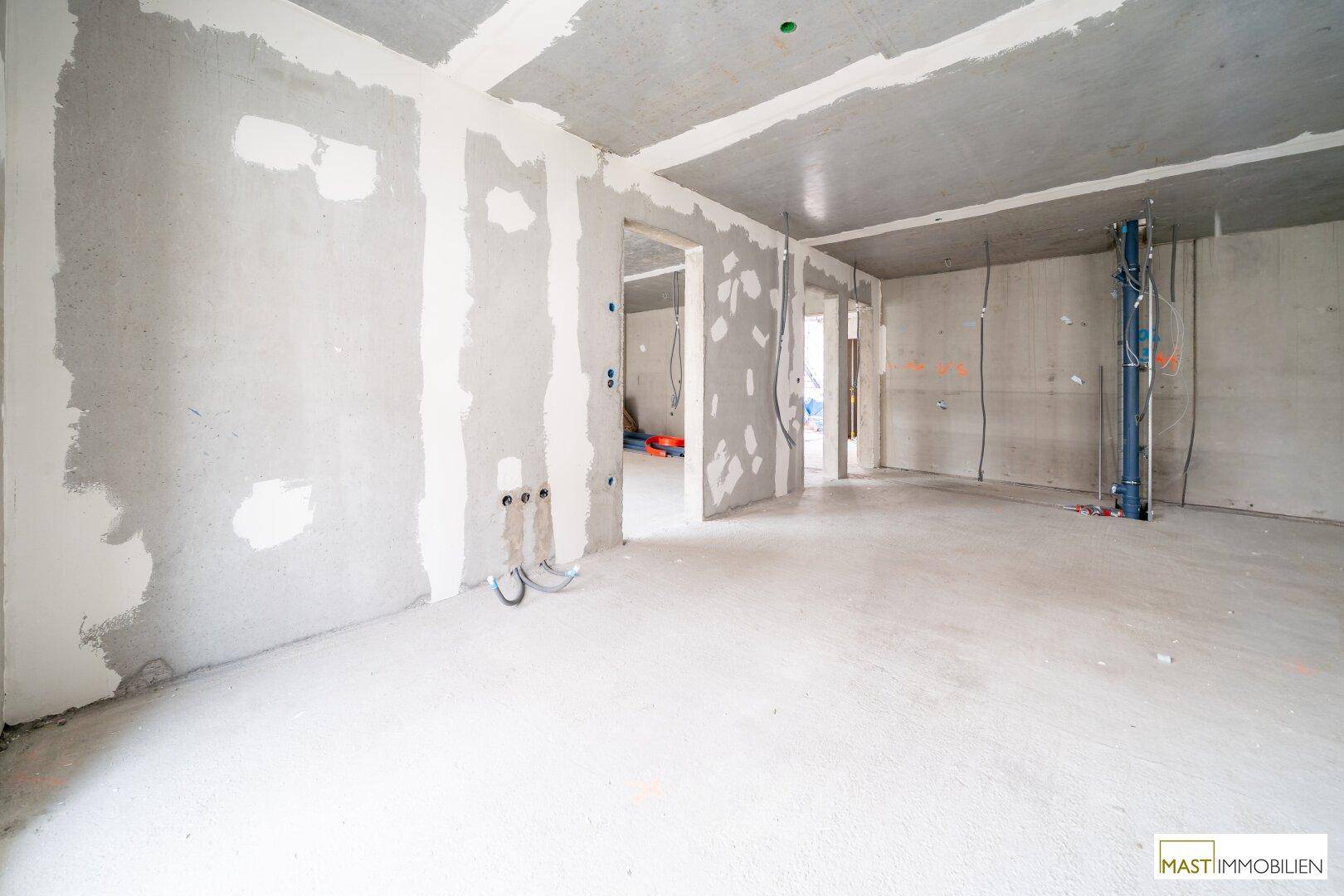 Unfertiger Innenraum im Rohbauzustand mit sichtbaren Installationen und Betonoberflächen.
