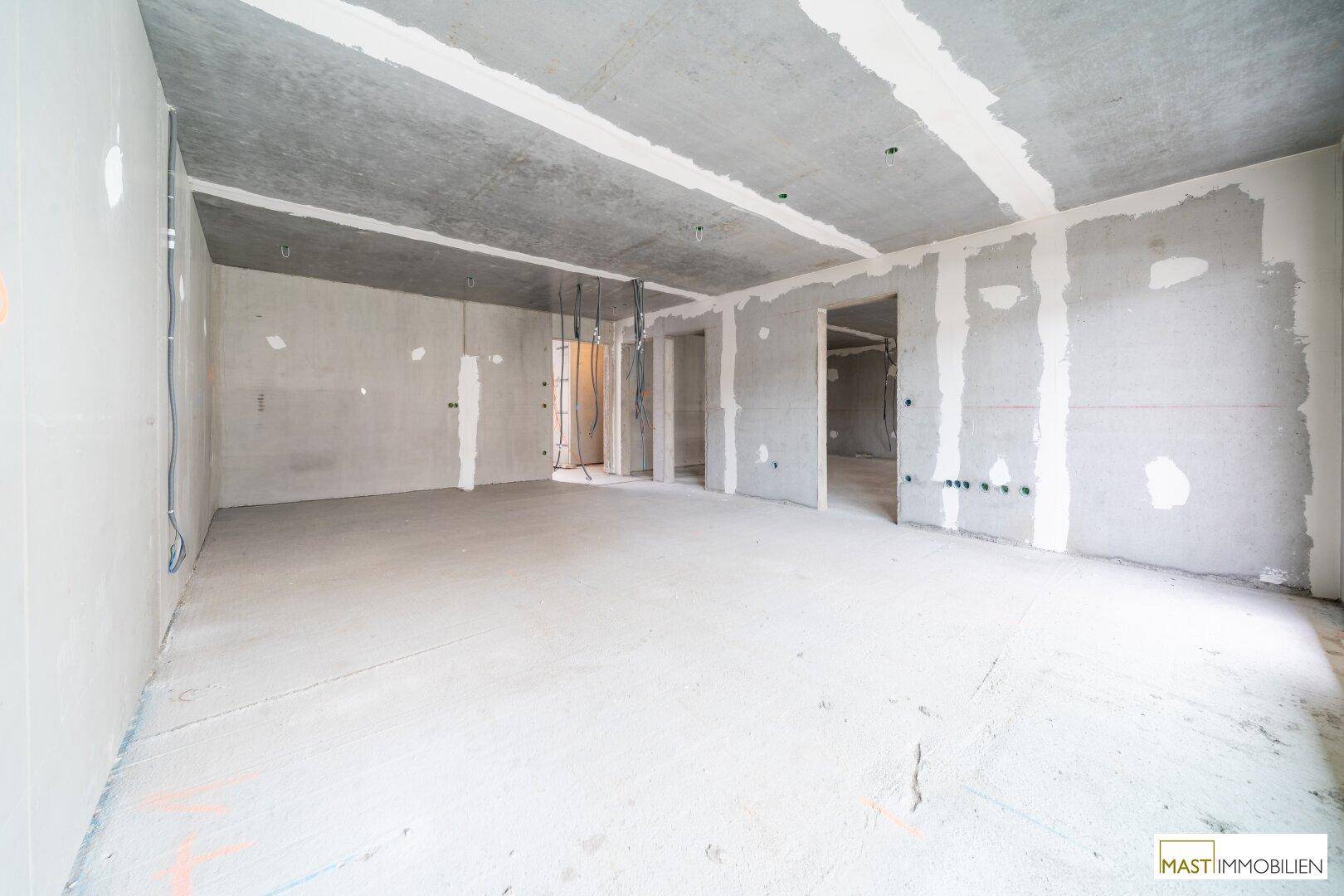 Geräumiger Innenraum im Rohbau mit Betonwänden und Decken, bereit für den Ausbau.