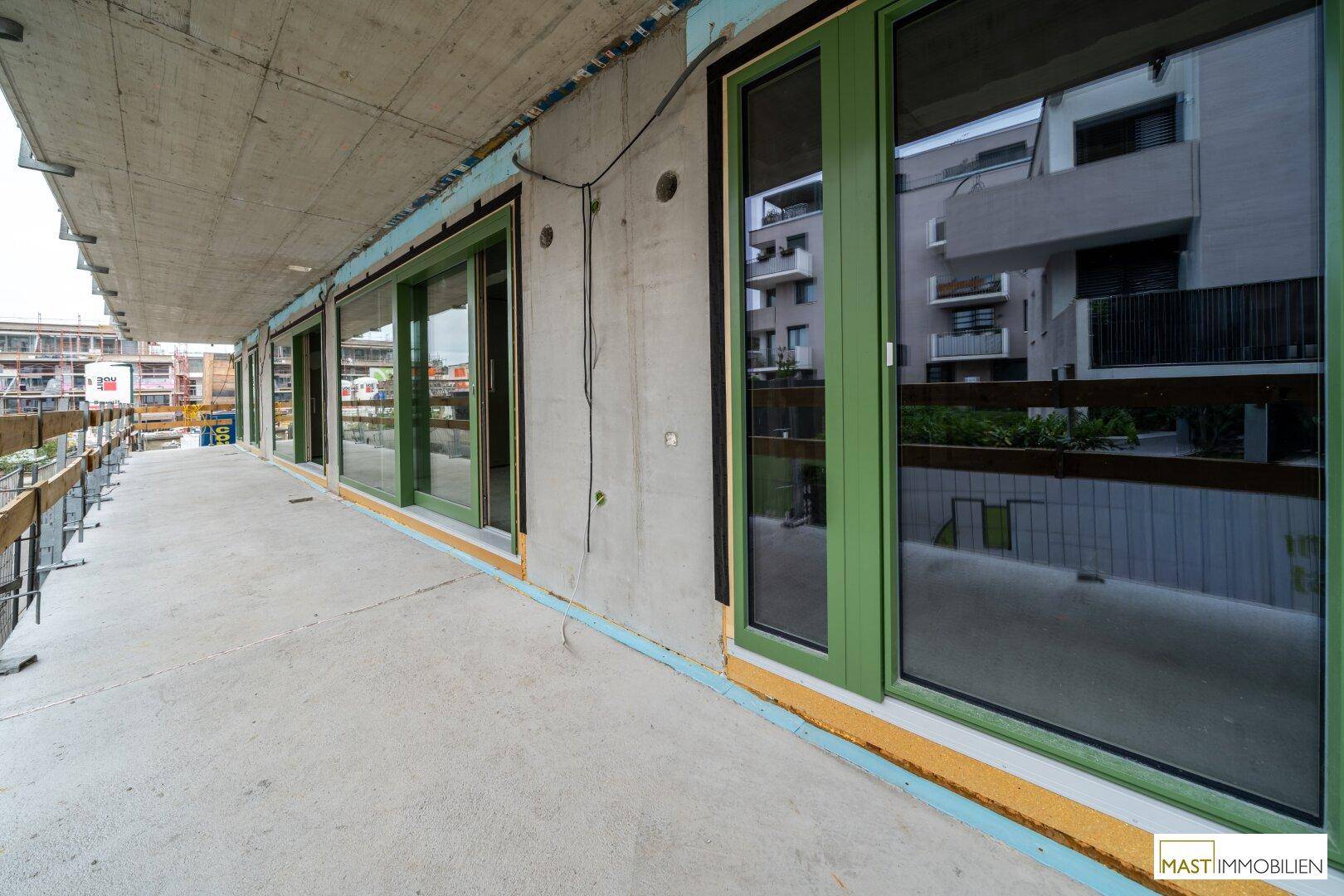 Unfertiger Balkonbereich mit grünen Fensterrahmen und Blick auf die Baustelle.