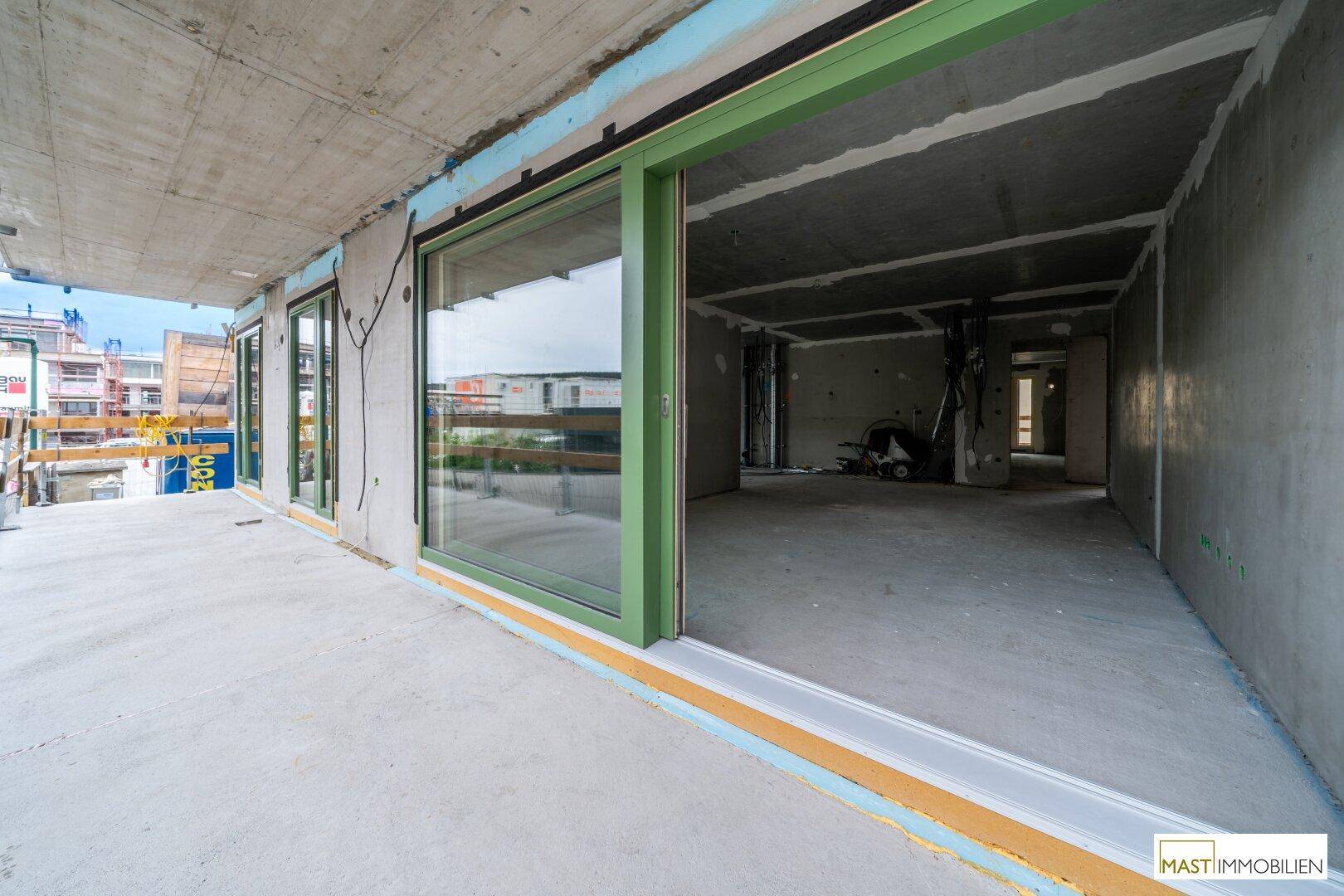 Unfertige Terrasse mit Schiebetüren, die Zugang zu einem Rohbau-Innenraum bieten.