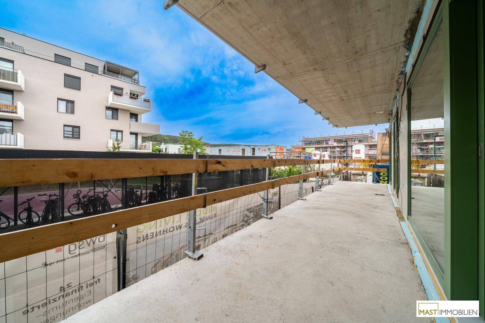 Lange, unfertige Terrasse mit provisorischem Geländer und Blick auf die umliegenden Gebäude.