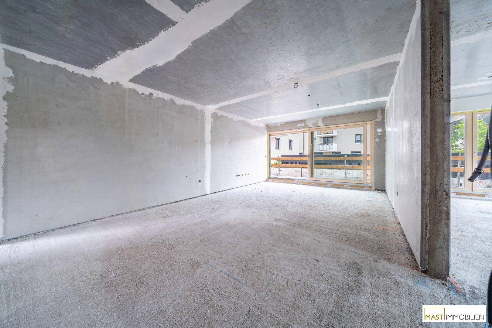 Heller Rohbau-Innenraum mit großen Fenstern, die viel Tageslicht hereinlassen.