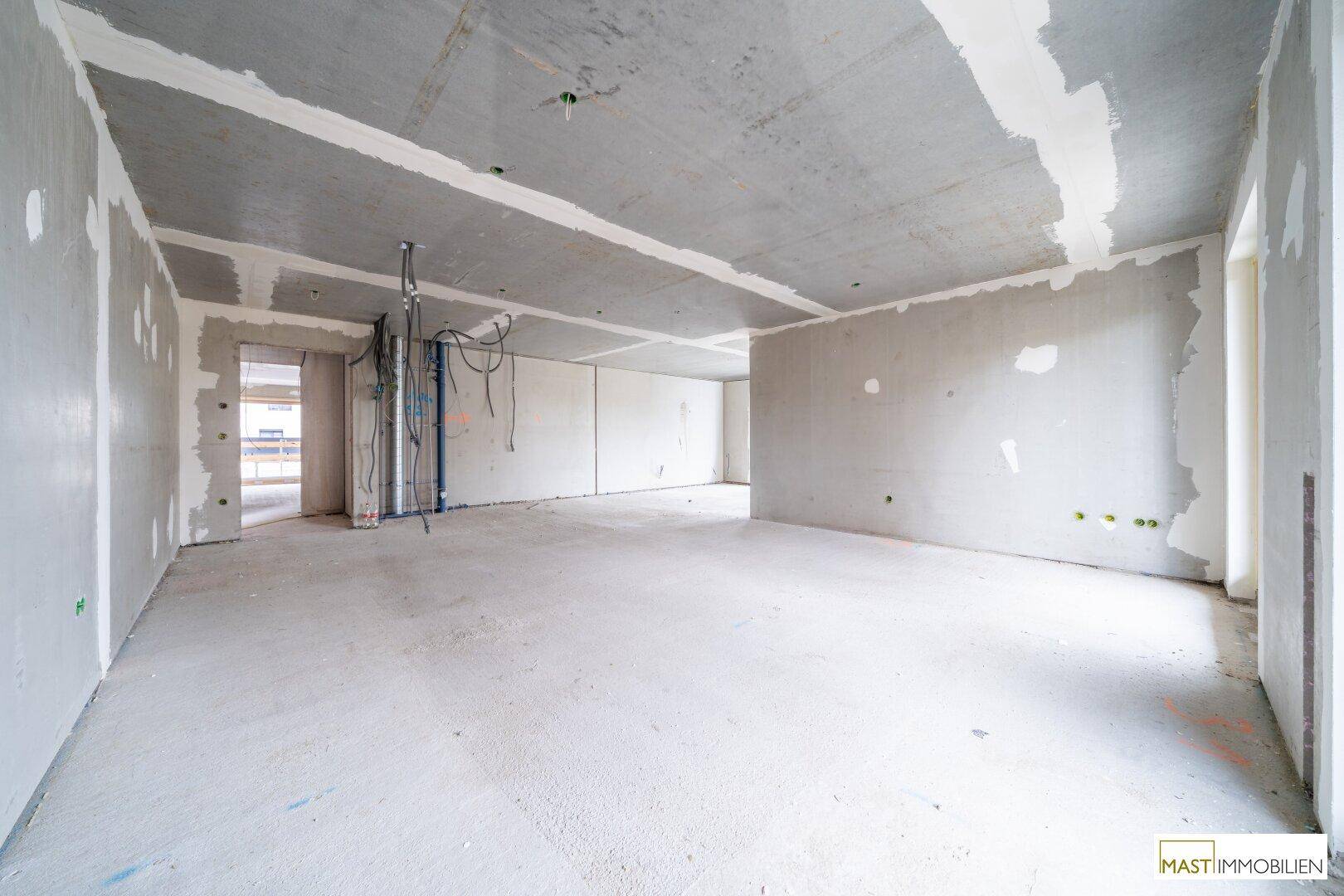 Unfertiger Innenraum mit sichtbaren Installationen und Rohbauwänden, bereit für den weiteren Ausbau.