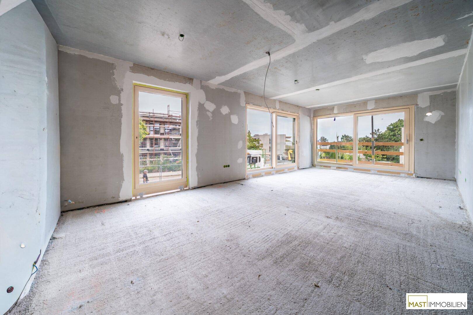 Heller Rohbau-Raum mit großen Fensterfronten, die viel Tageslicht hereinlassen.