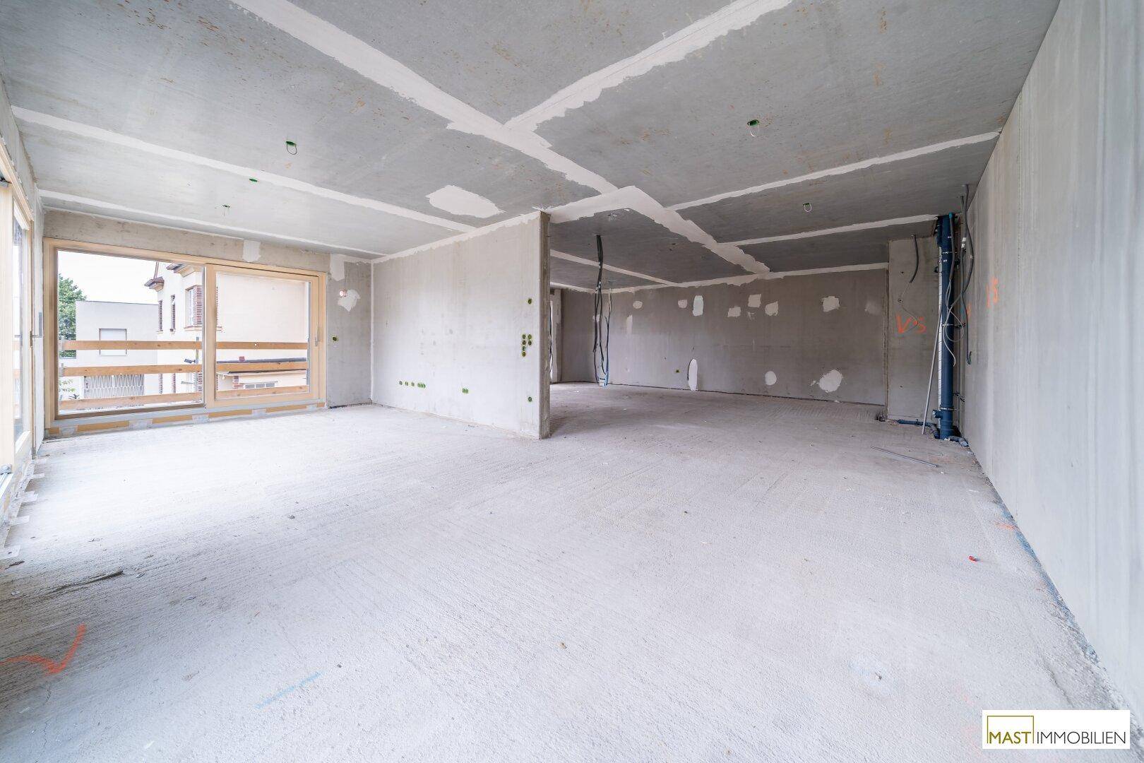 Geräumiger Rohbau-Innenraum mit Betonoberflächen und vorbereiteten Wandstrukturen.