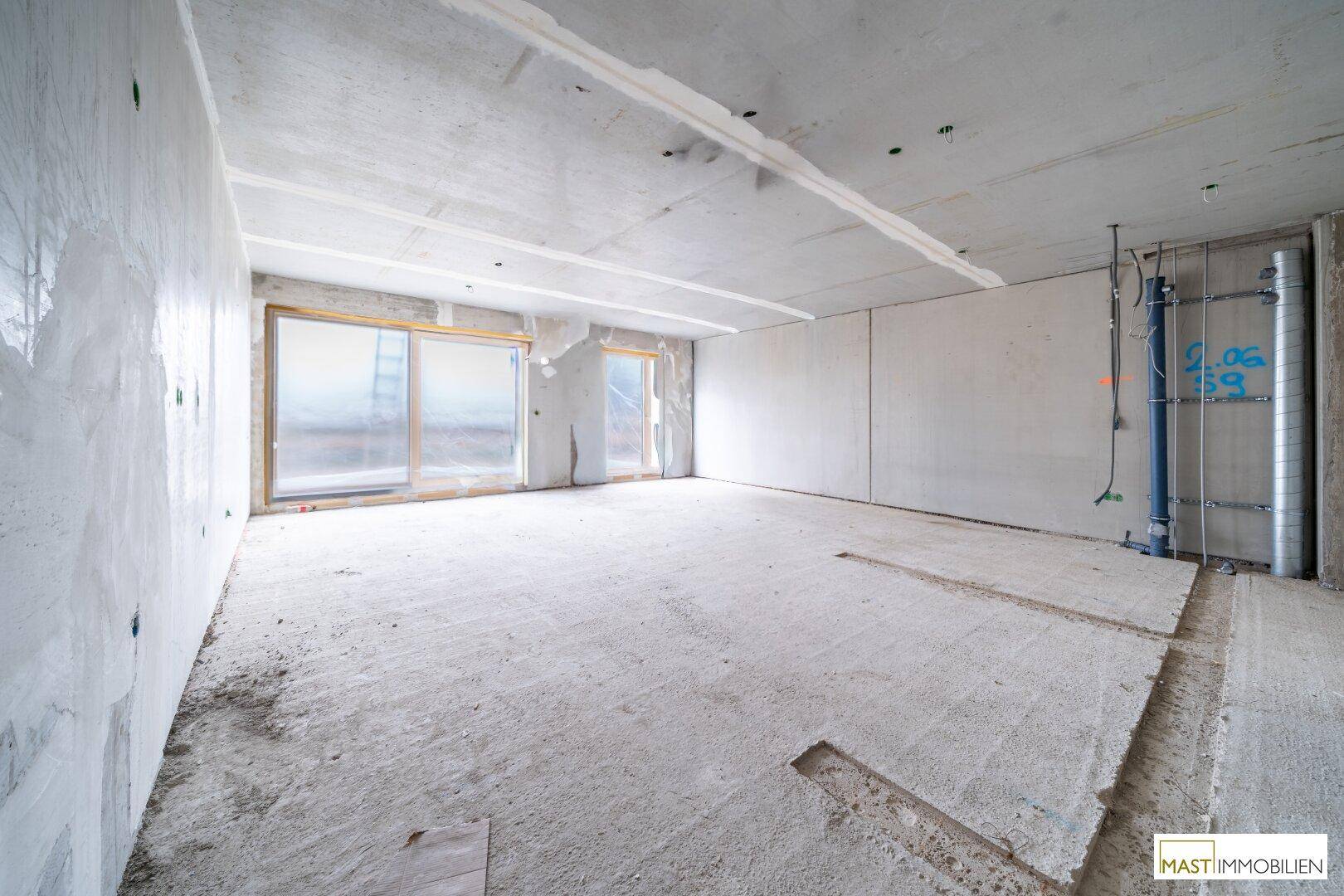 Unfertiger Innenraum im Rohbauzustand mit großen Fenstern und Betonwänden.