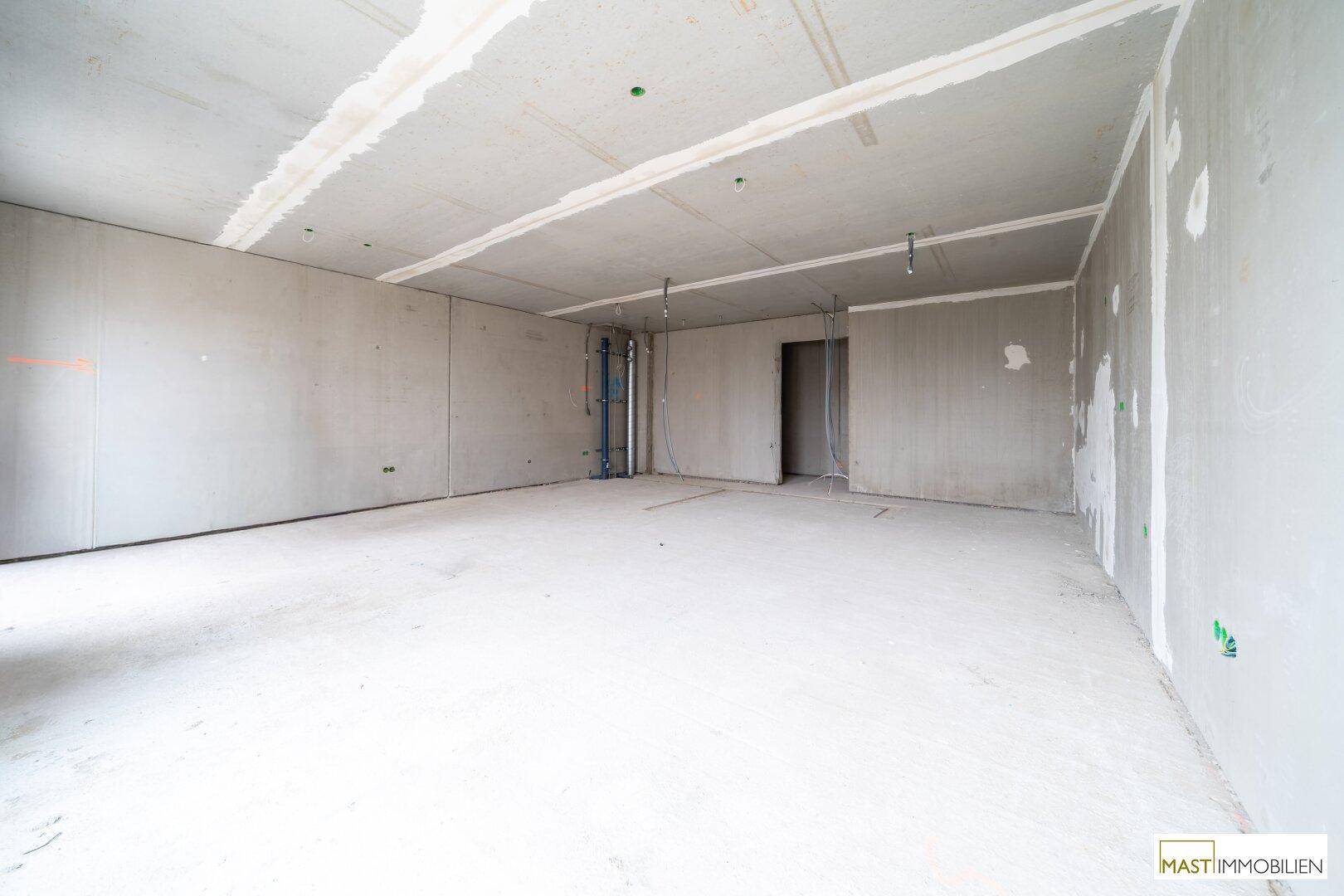 Leerer Innenraum im Rohbau mit Betonoberflächen und Türöffnung.