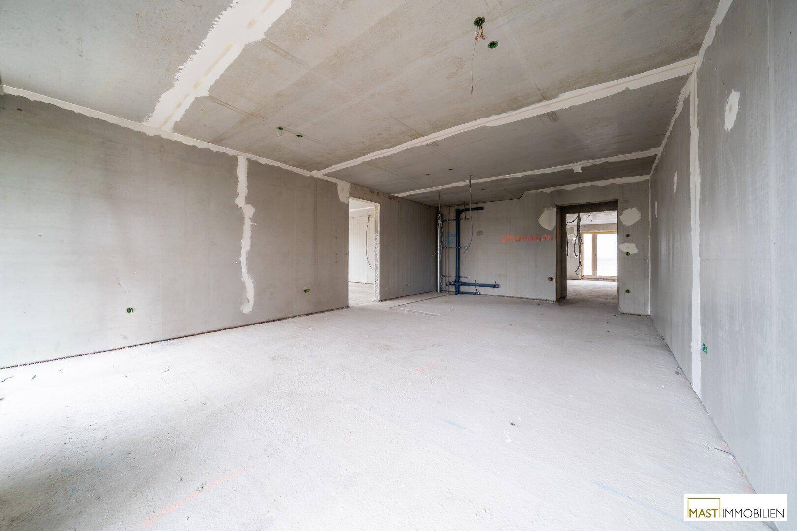Unfertiger Innenraum im Rohbau mit sichtbaren Installationen und Betonboden.