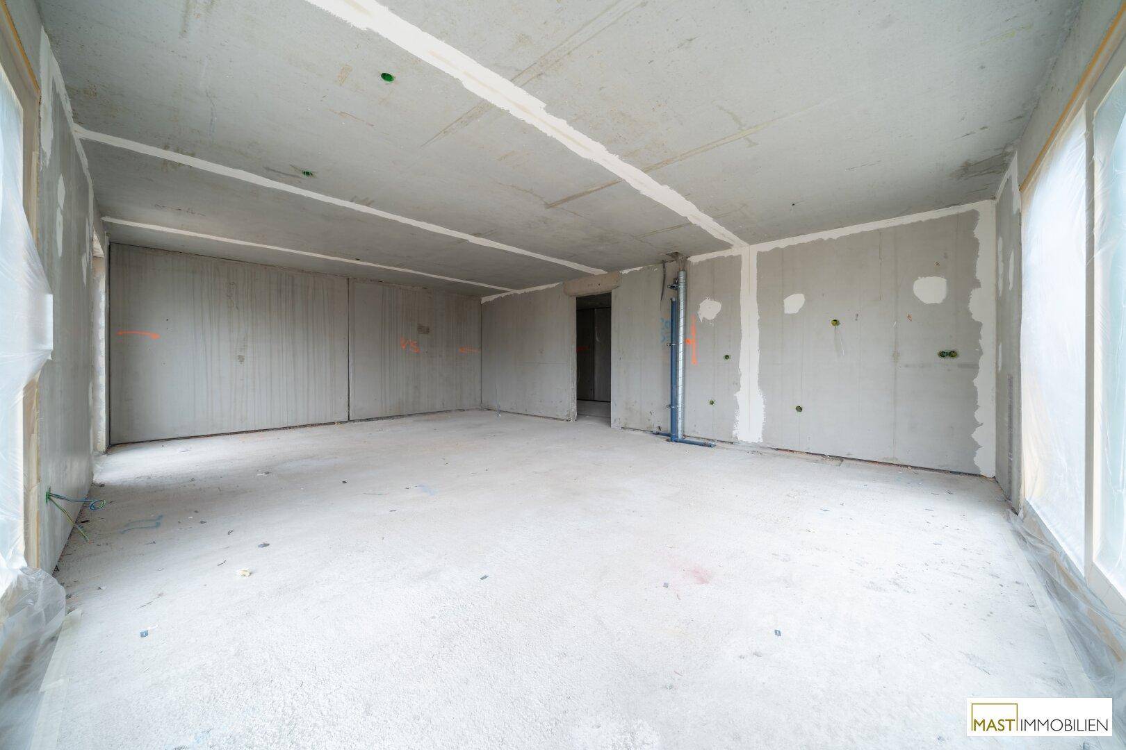 Leerer Rohbau eines Raumes mit Betonboden und vorbereiteten Wänden.