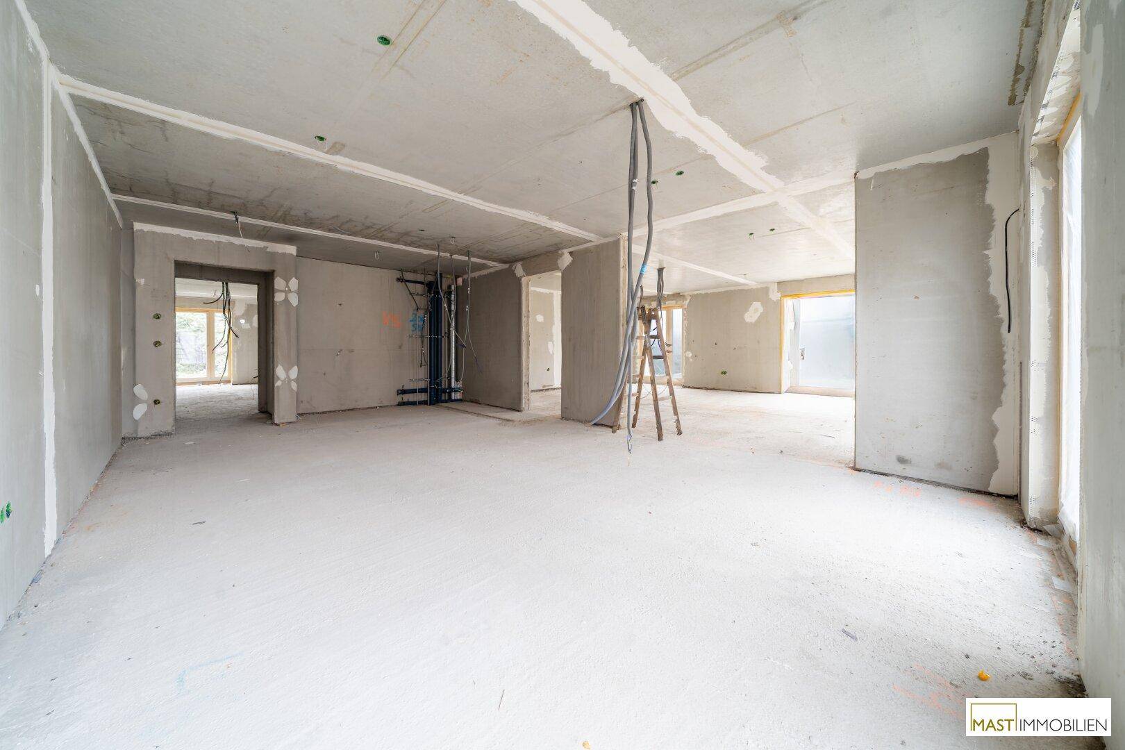 Rohbau-Innenraum mit Betonoberflächen, vorbereiteten Installationen und viel Tageslicht durch die Fenster.