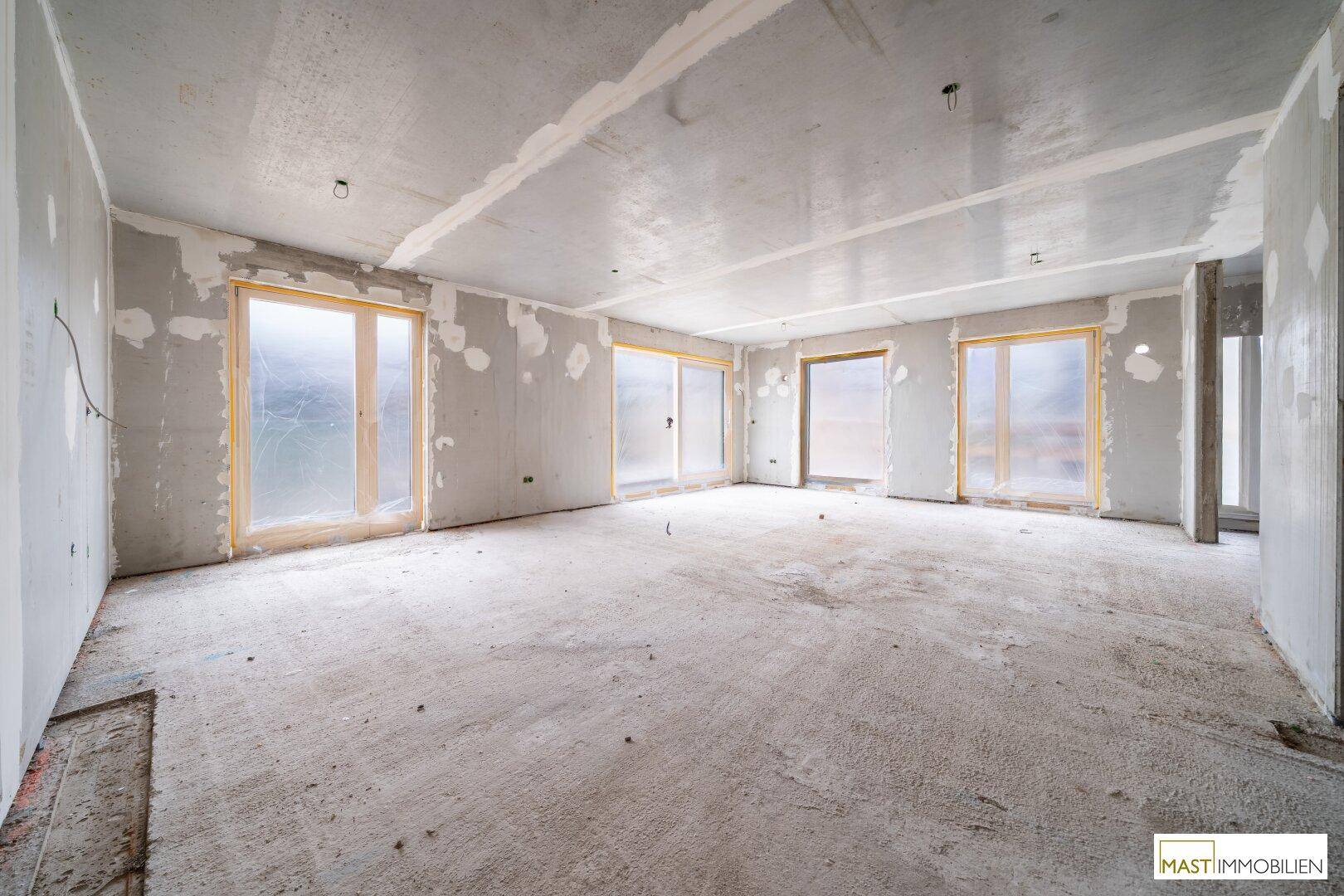 Geräumiger Rohbau-Innenbereich mit großen Fensteröffnungen und unverputzten Betonwänden und -boden.