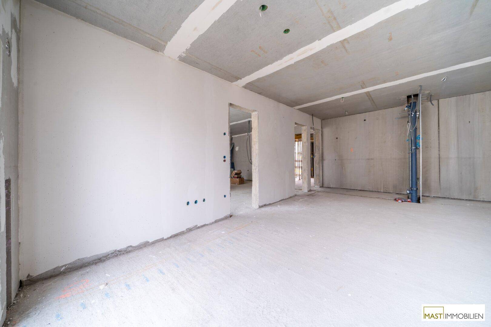 Unfertiger Innenraum im Rohbauzustand mit Betonboden und -decke sowie vorbereiteten Wänden.