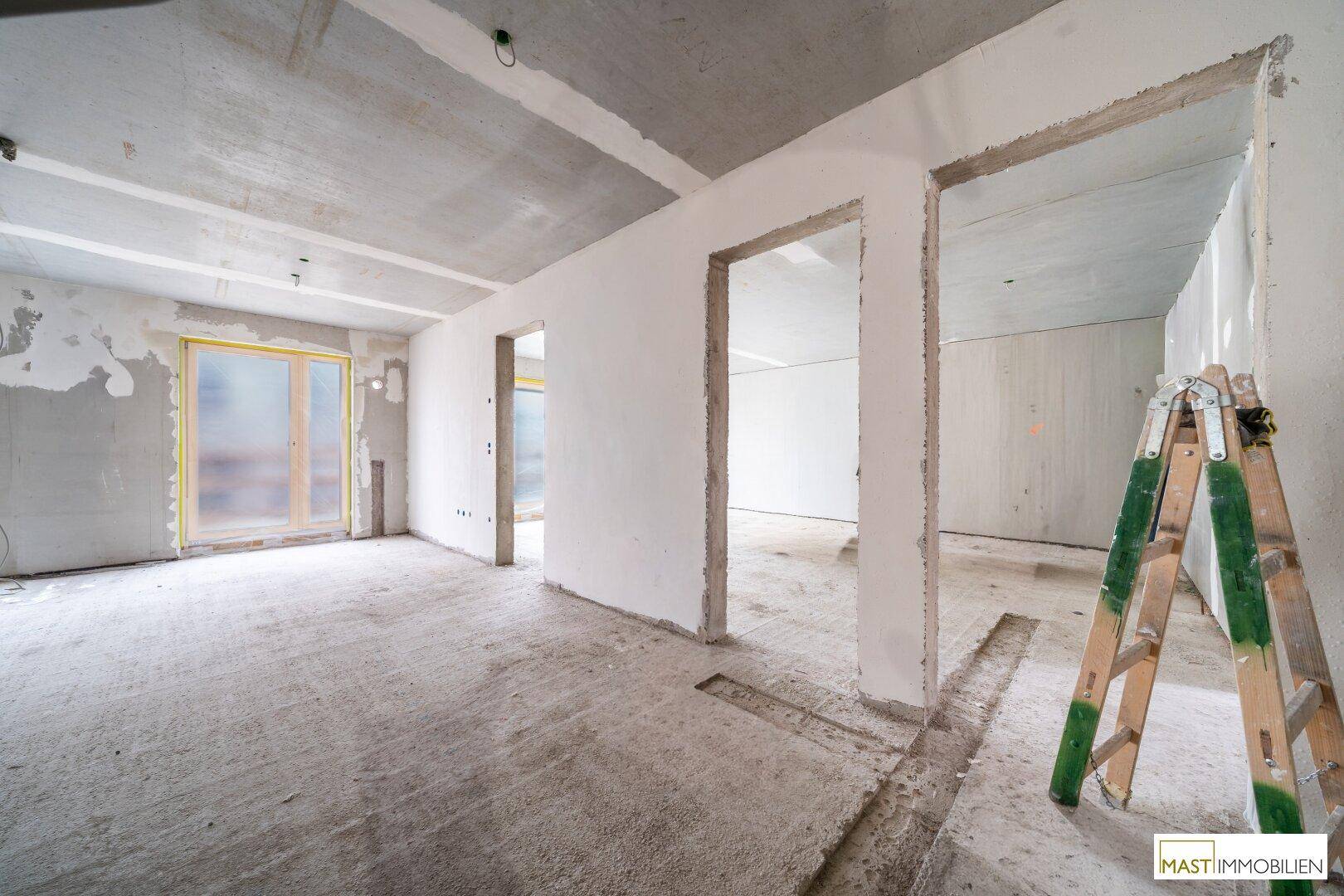 Rohbau eines Innenraums mit Betonboden, unverputzten Wänden und einem Fenster mit Schutzfolie.