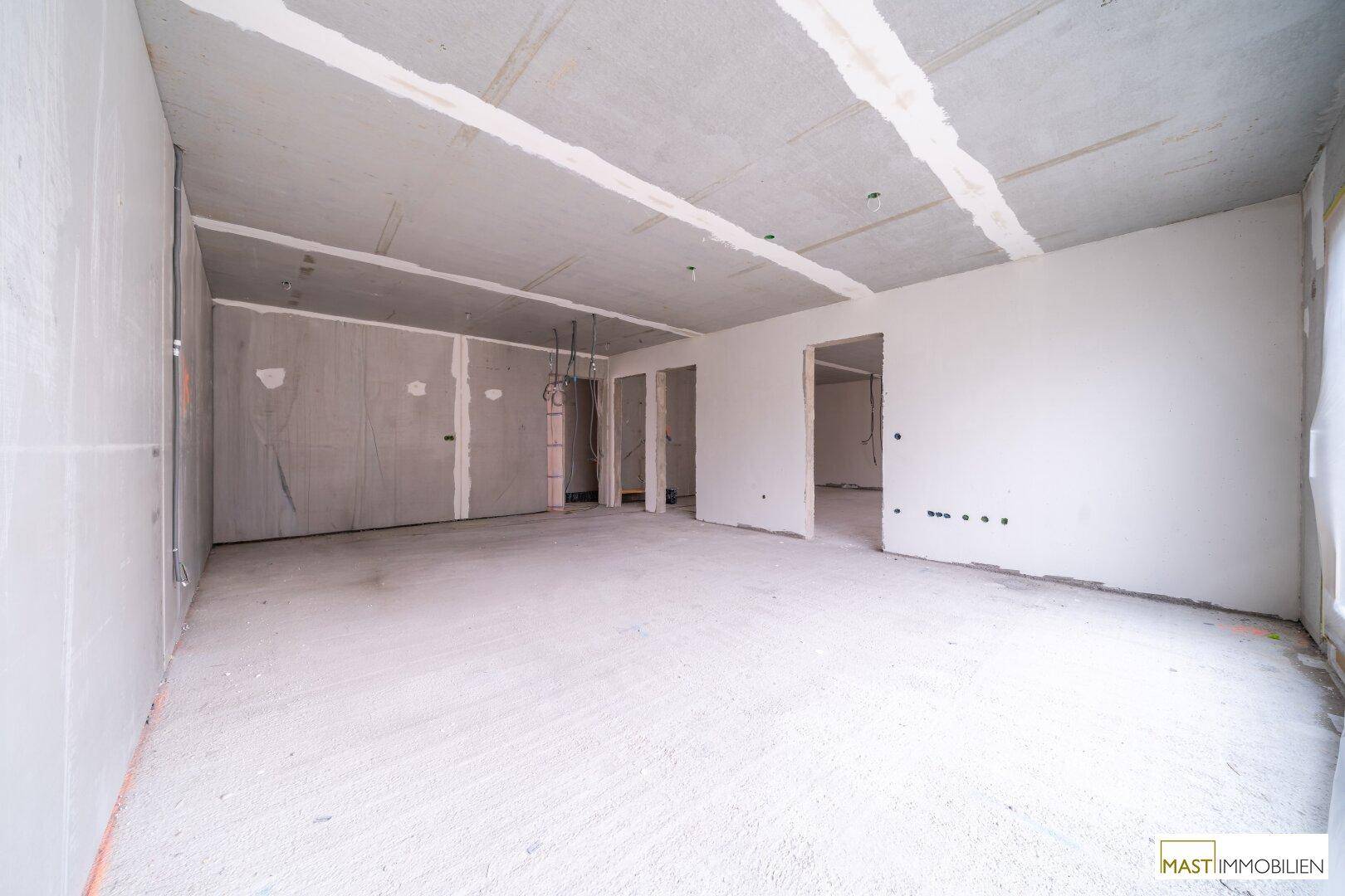 Leerer Innenraum im Rohbau mit Betonboden, unverputzten Wänden und mehreren Türöffnungen.