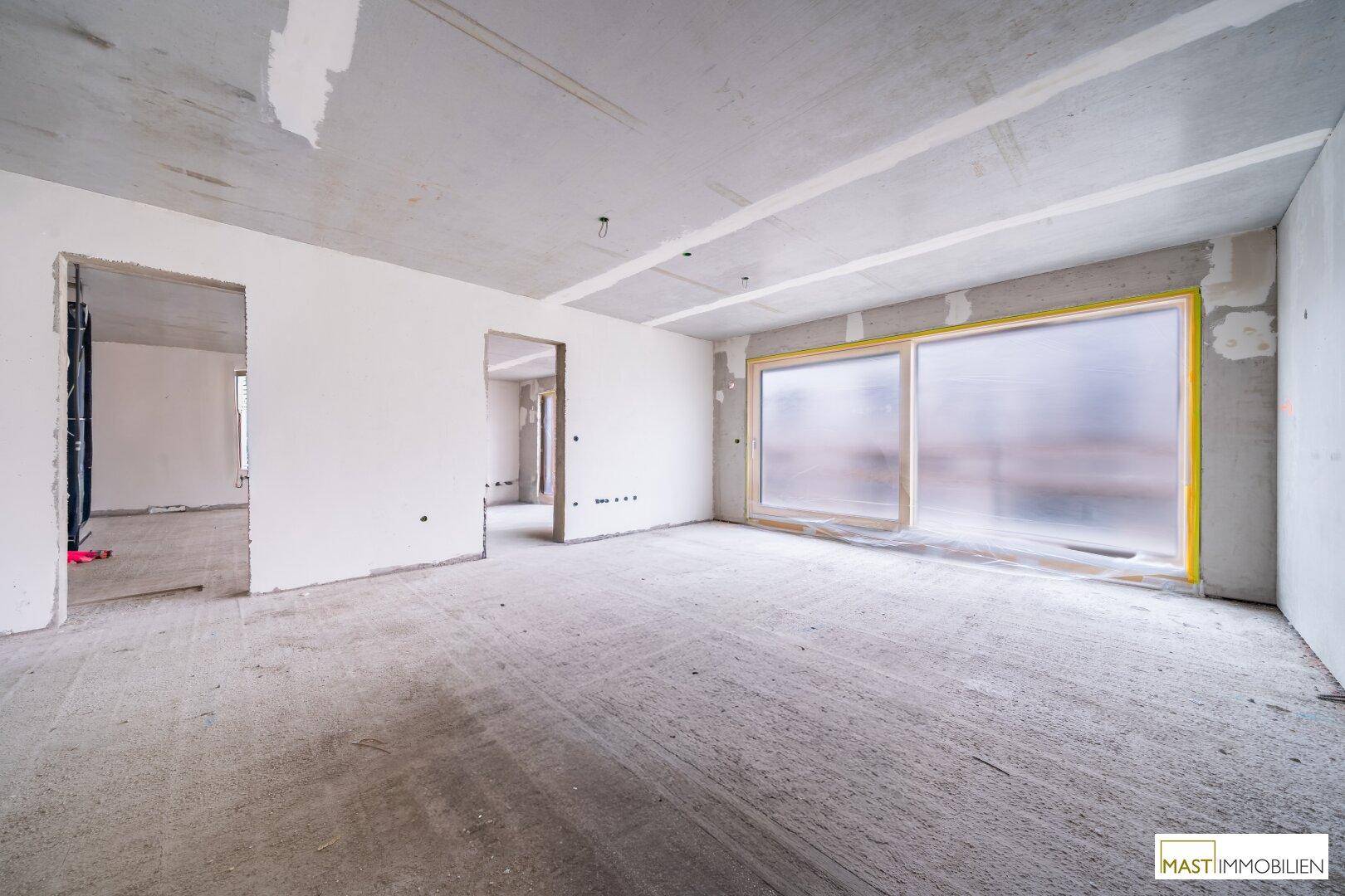 Rohbau eines Raumes mit Betonboden, unverputzten Wänden und einem großen, geschützten Fenster.