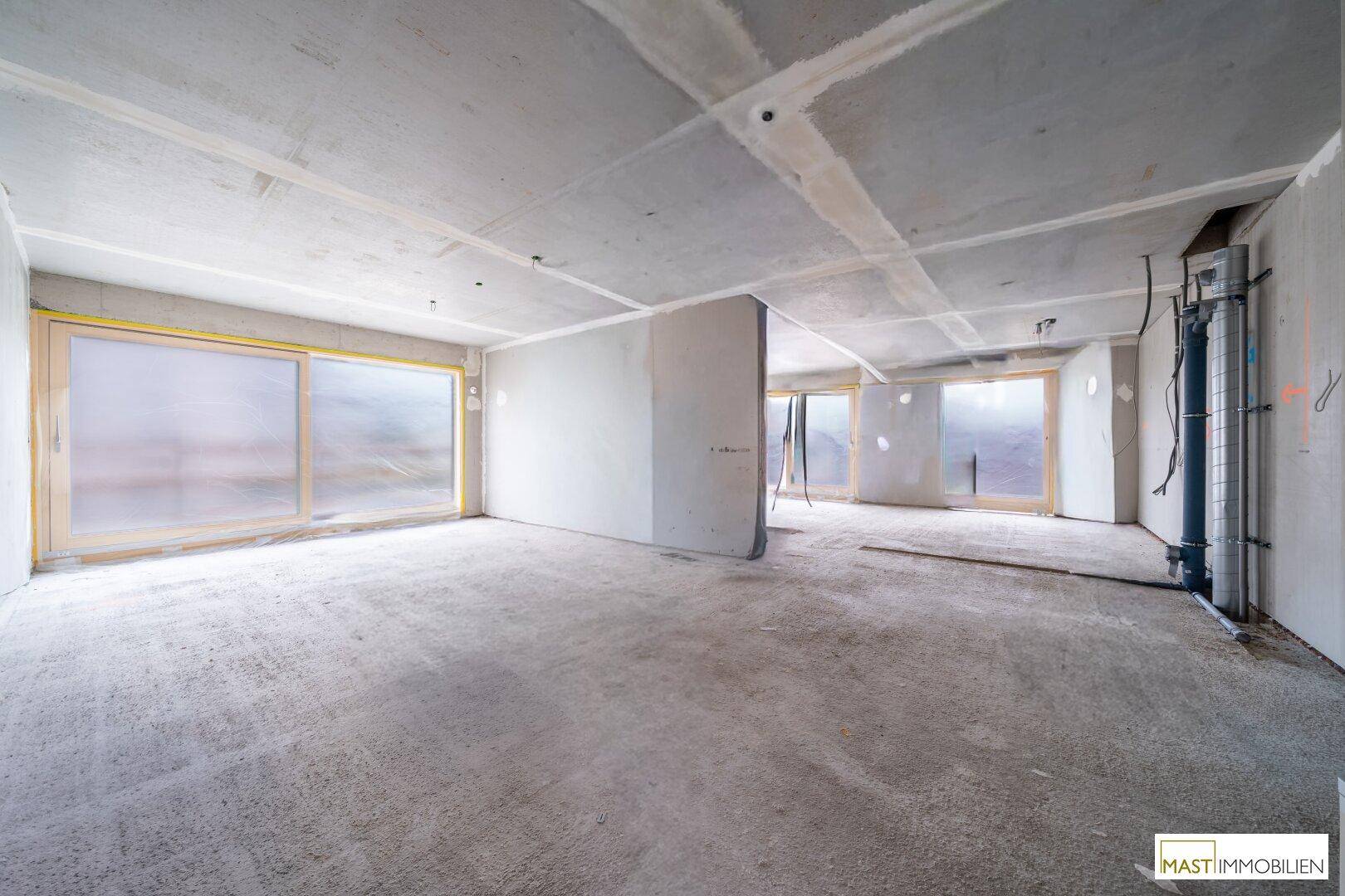 Unfertiger Innenraum mit Betonboden und großen Fenstern, bereit für den weiteren Ausbau.
