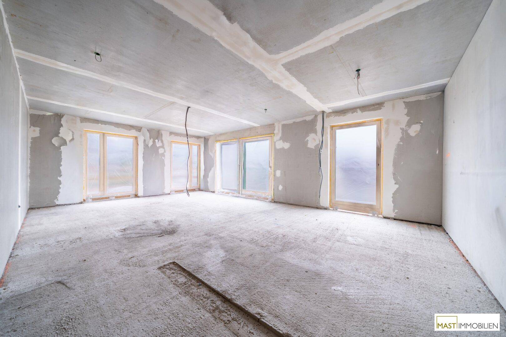 Heller Rohbau eines Zimmers mit Betonboden und mehreren Fensteröffnungen für viel Tageslicht.