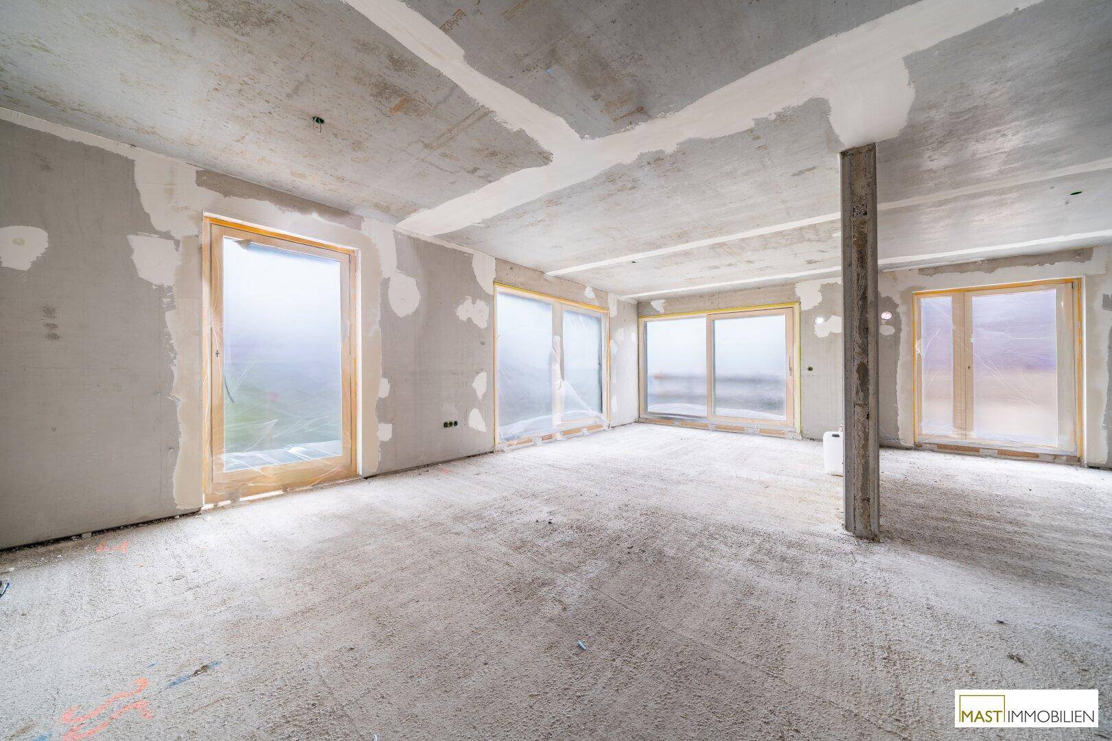 Geräumiger Rohbau-Innenraum mit großen Fenstern und Betonstütze, wartet auf Fertigstellung.