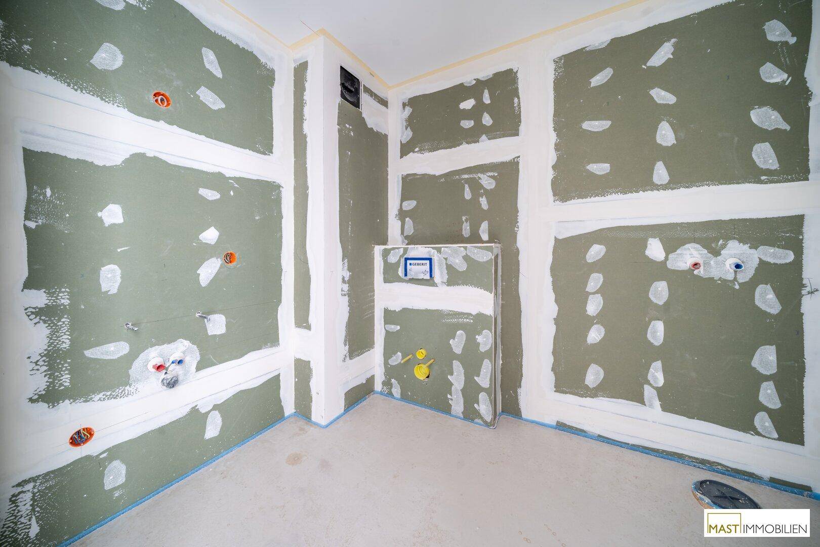 Badezimmer im Rohbau mit vorbereiteten Anschlüssen für Sanitärinstallationen und Wand-WC-Rahmen.
