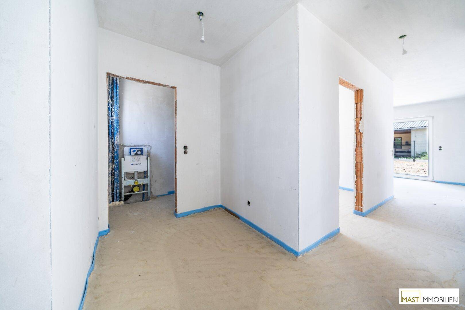 Unfertiger Raum, wahrscheinlich ein Gäste-WC, mit sichtbaren Sanitärinstallationen und Rohbetonboden.