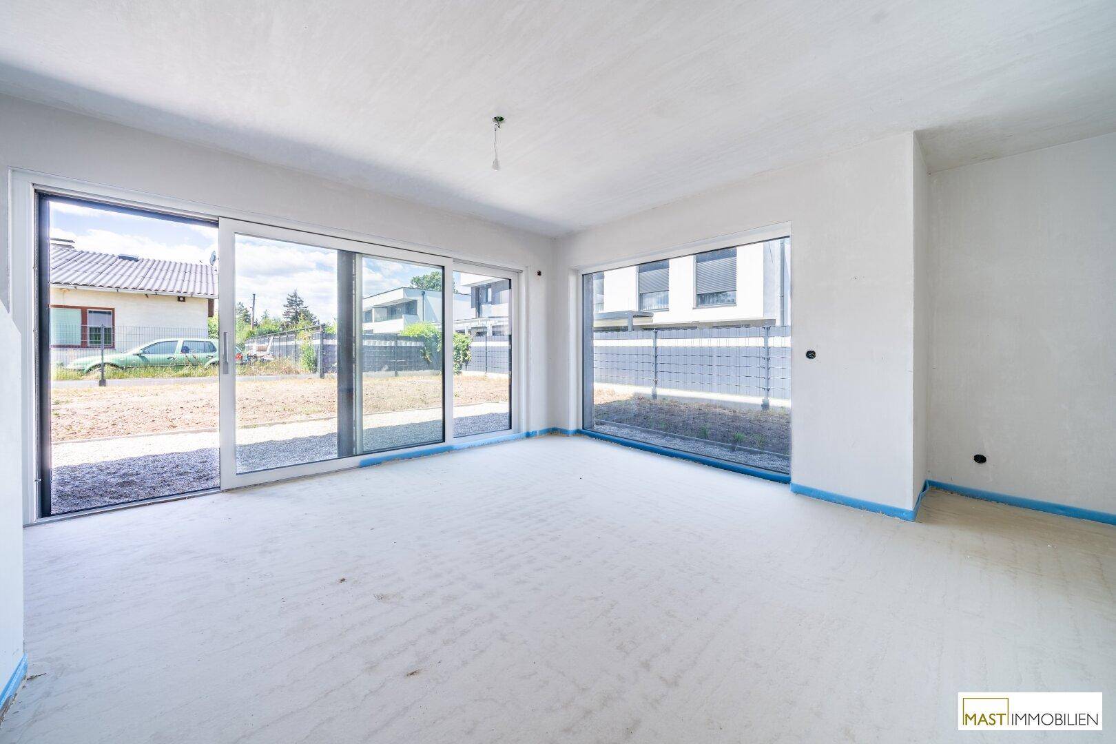Heller, unfertiger Wohnraum mit großen Fensterfronten und Schiebetüren, die den Blick ins Grüne freigeben.