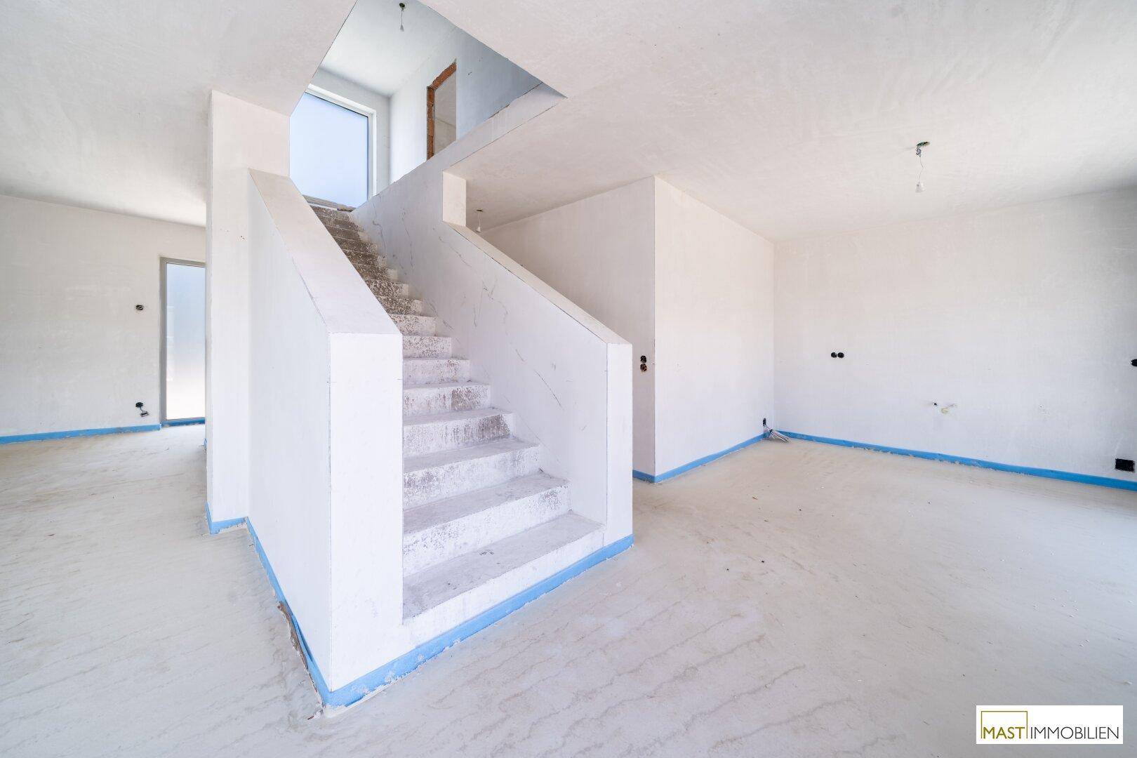 Heller, unfertiger Wohnraum mit einer markanten Treppe und einem Fenster im oberen Bereich für zusätzliches Licht.