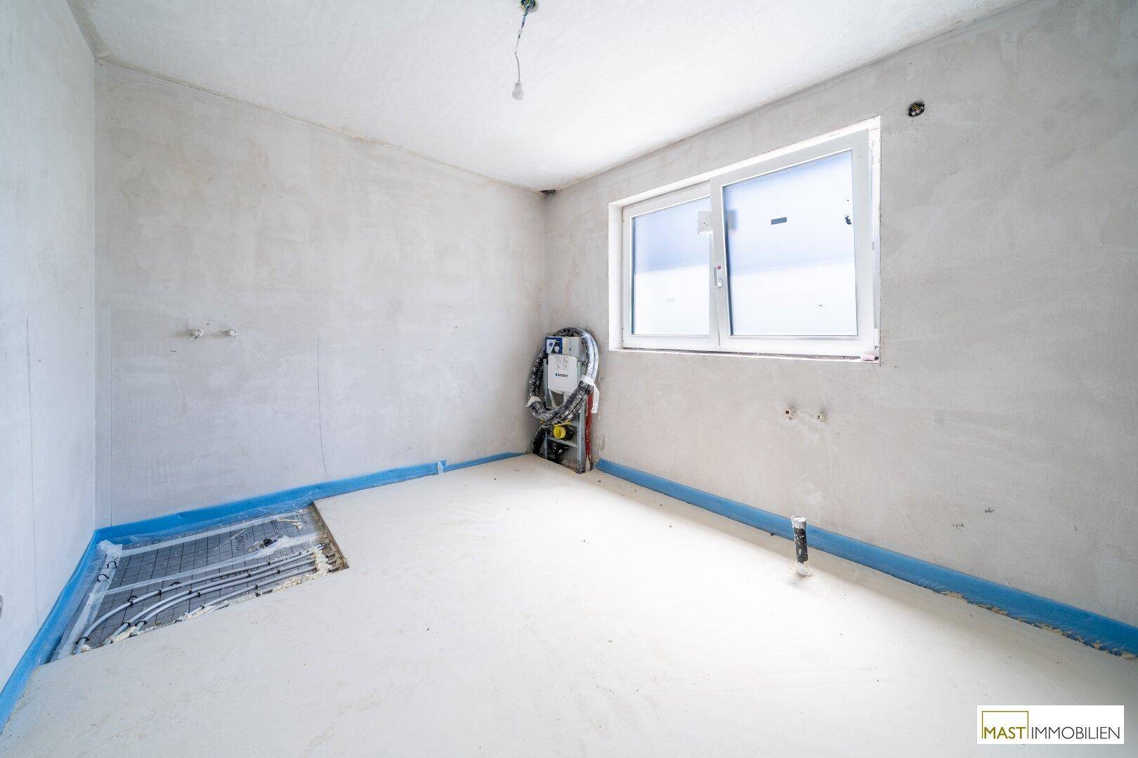 Unfertiges Badezimmer mit sichtbaren Installationen für Sanitäranlagen und einem Fenster für natürliche Belüftung.