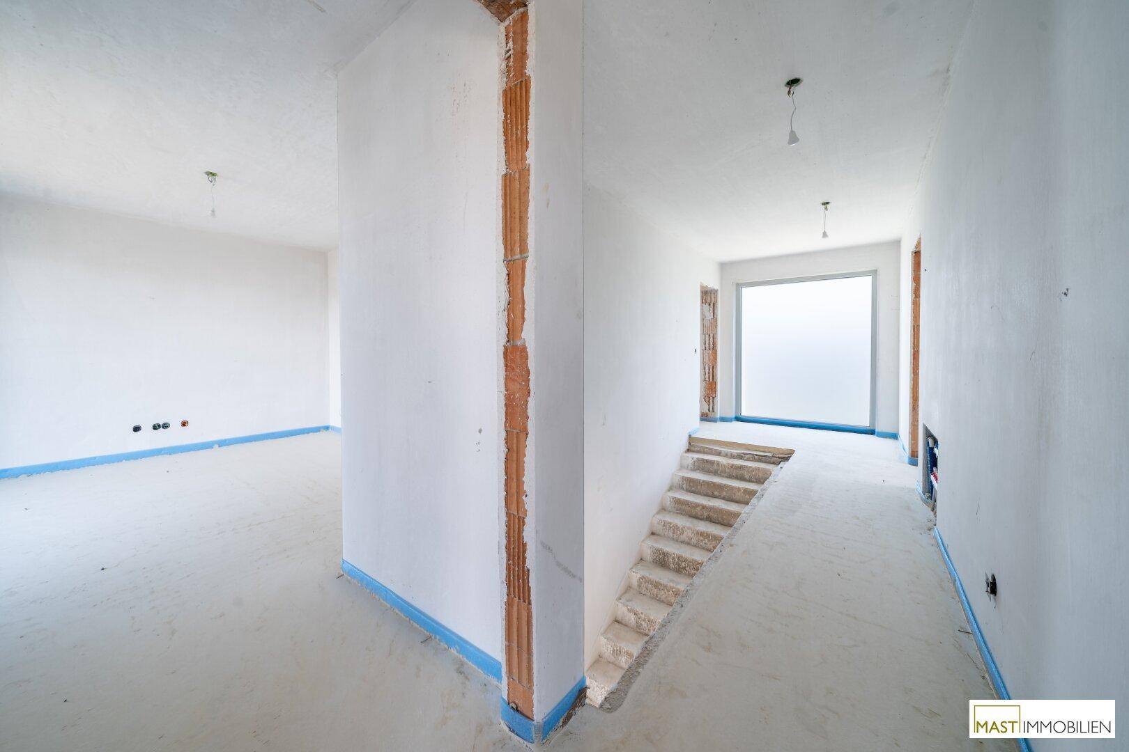 Unfertiger Flurbereich mit Treppenansatz und weiß verputzten Wänden, bereit für den weiteren Ausbau.
