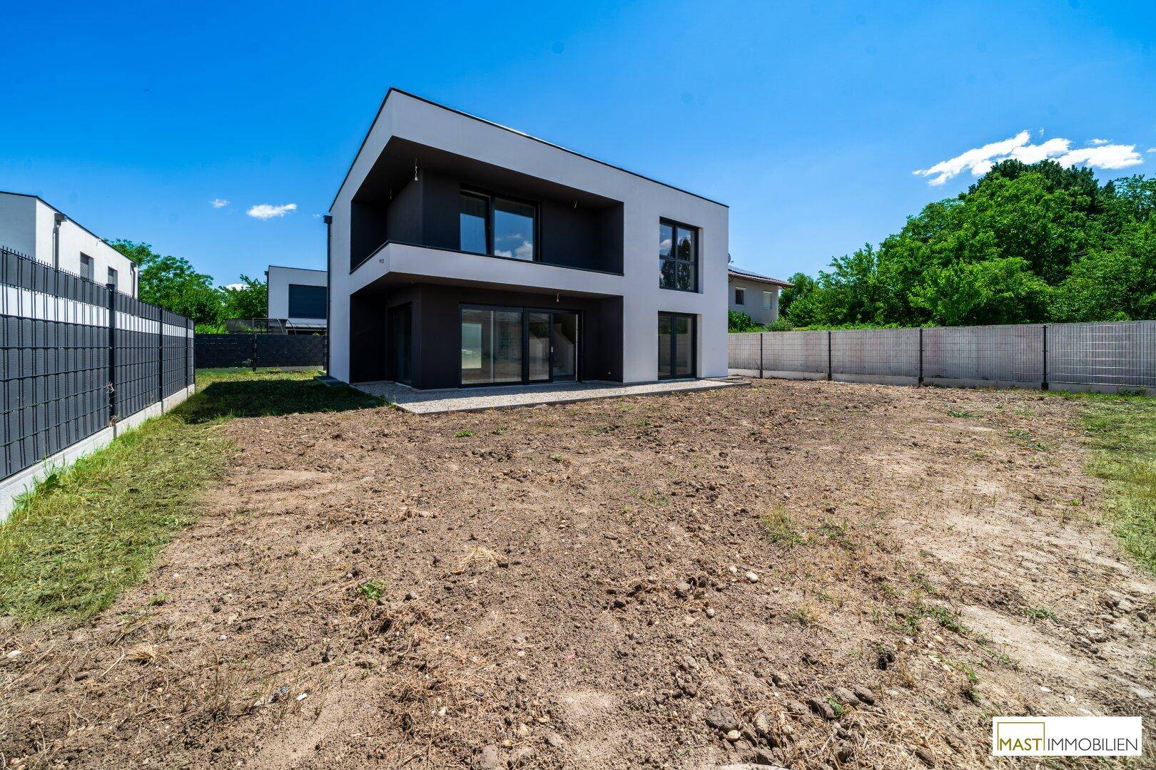Modernes Einfamilienhaus mit klarer Linienführung und großem, noch unbebautem Grundstück unter blauem Himmel.
