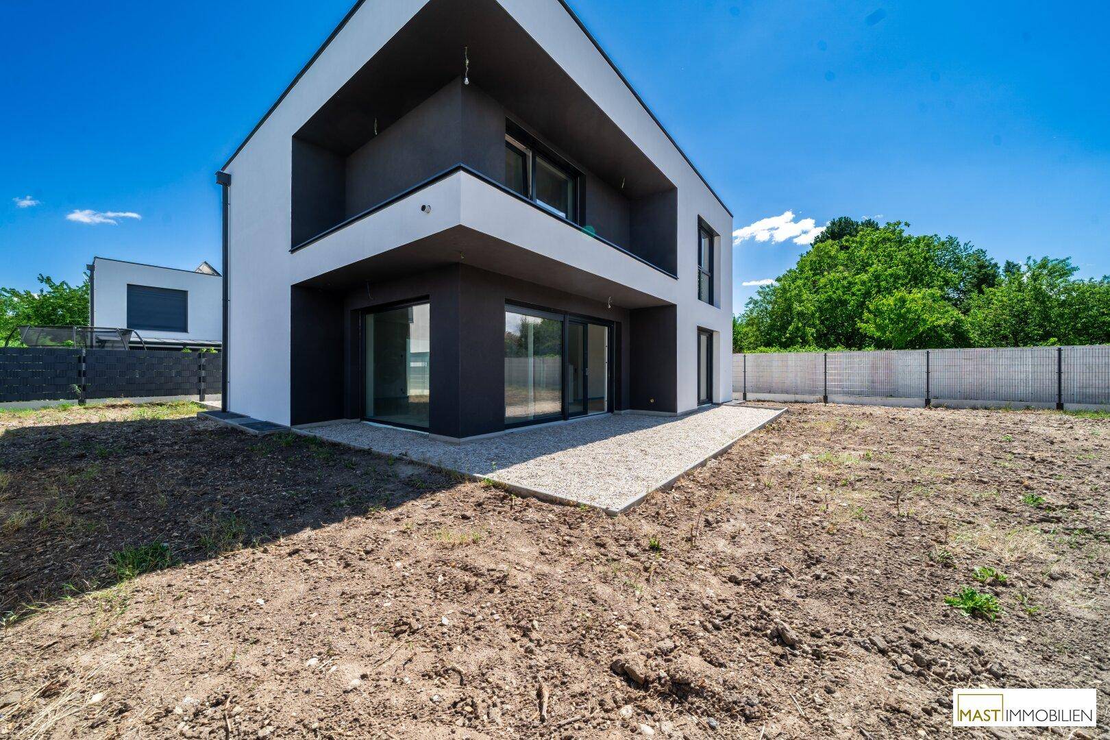 Seitenansicht eines modernen Neubaus mit einer kleinen Kiesfläche neben dem Gebäude und unbebautem Gartenbereich.