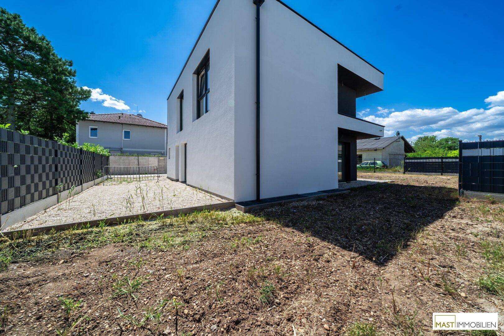 Seitenansicht des modernen Hauses mit einem Kiesweg und dem noch ungestalteten Gartenbereich.