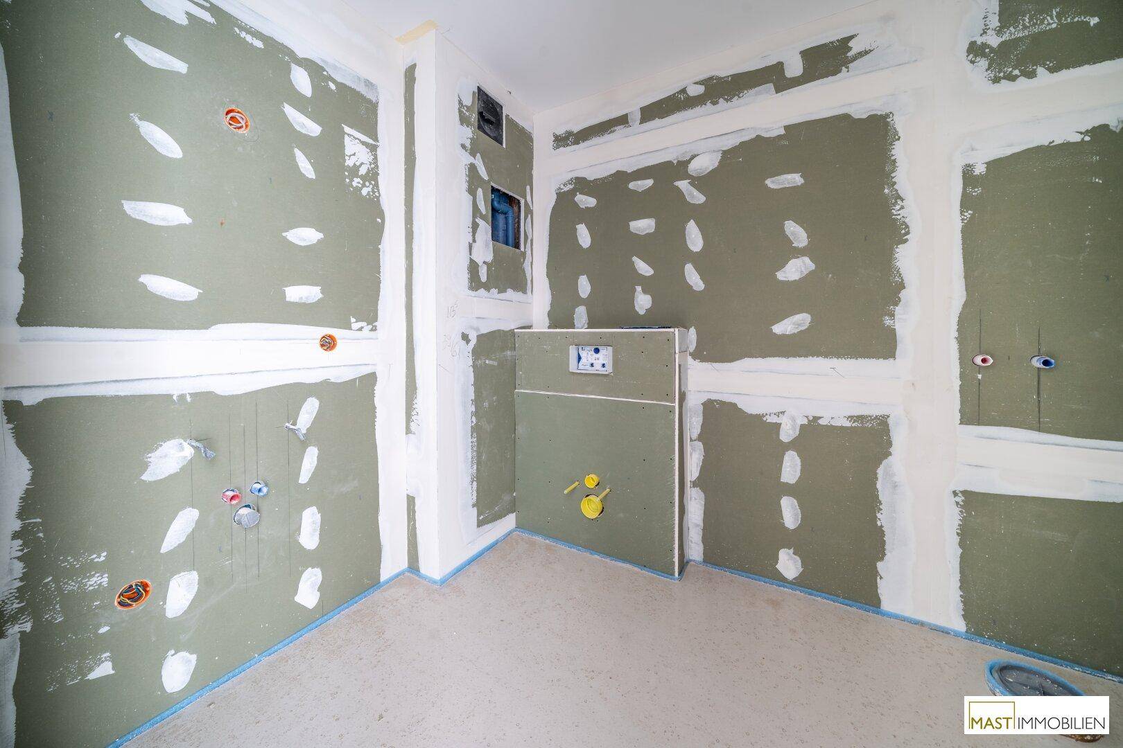 Unfertiges Badezimmer mit vorbereiteten Installationen für Toilette und Waschbecken.