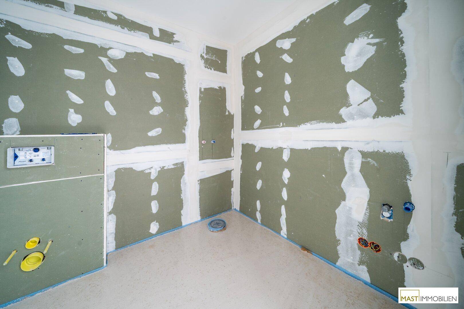 Rohbau-Badezimmer mit vorbereiteten Anschlüssen für Sanitäranlagen und Trockenbauwänden.