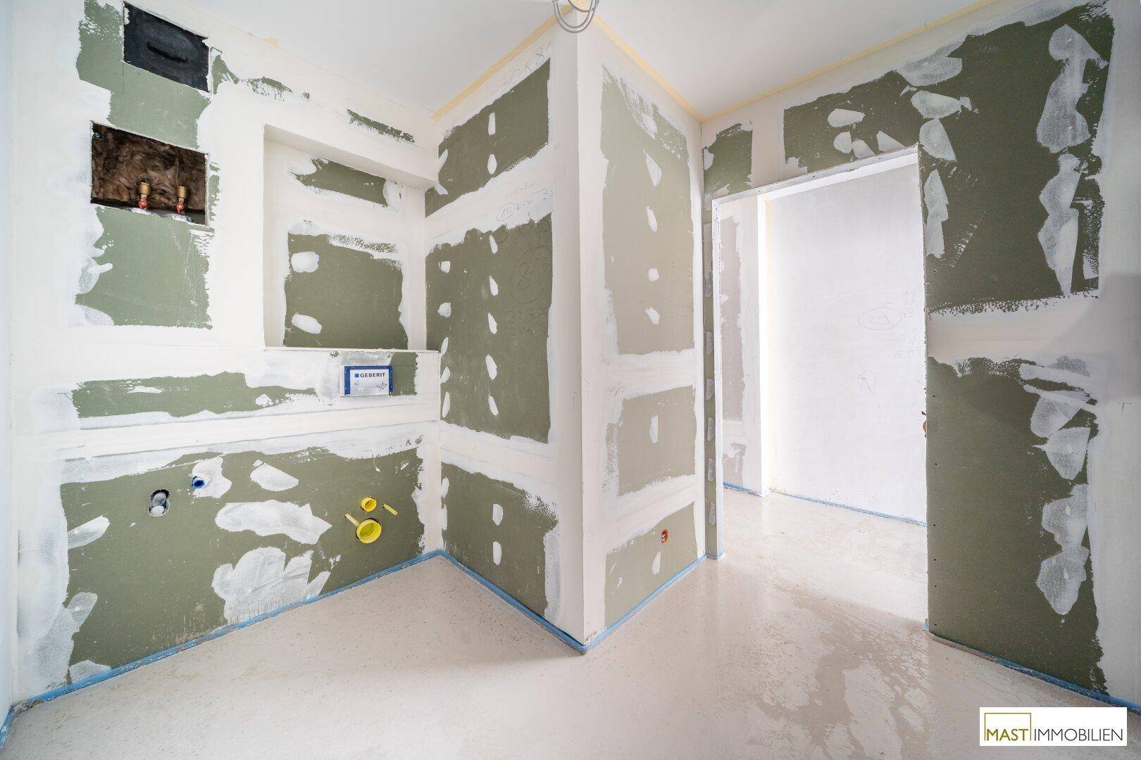 Rohbau-Badezimmer mit vorbereiteten Anschlüssen für Sanitäranlagen und unverputzten Wänden.