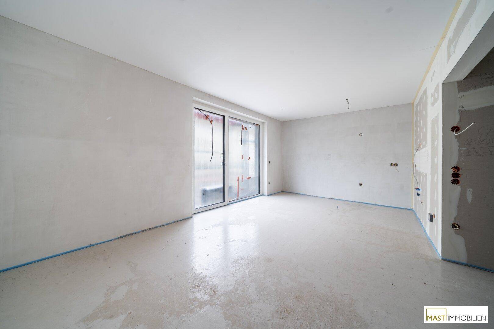 Unfertiger Innenraum mit Rohbauwänden, Estrichboden und großen Schiebetüren, bereit für den Ausbau.