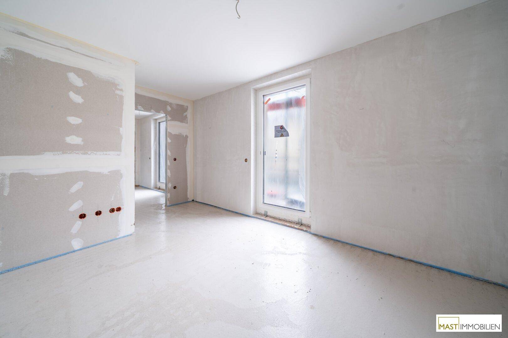 Unfertiger Raum im Neubau mit Trockenbauwänden und einem großen, abgedeckten Fenster.