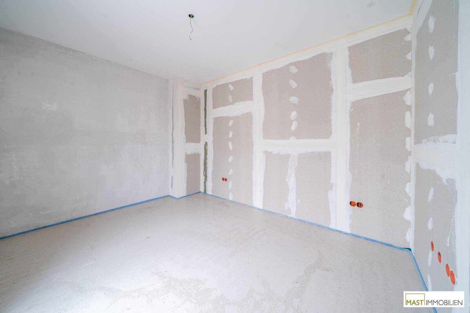 Rohbauzimmer mit vorbereiteten Trockenbauwänden und sichtbaren Elektroinstallationen.