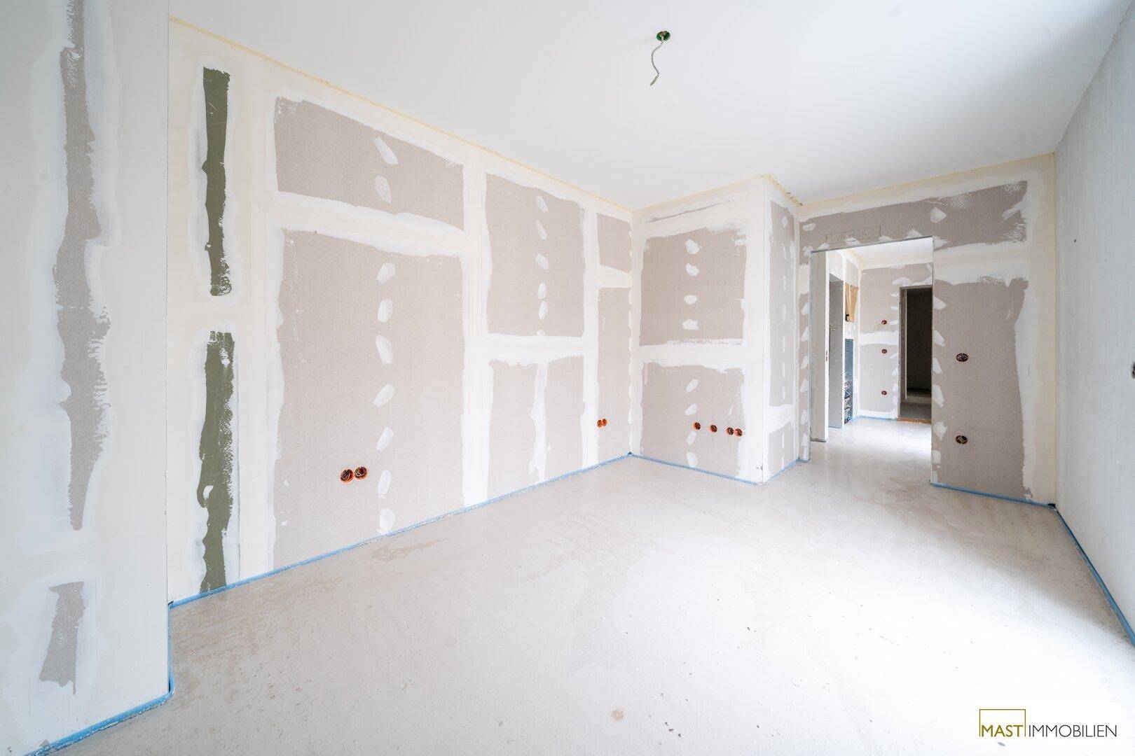 Innenraum im Rohbau mit Trockenbauwänden, Elektroinstallationen und Blick in angrenzende Bereiche.