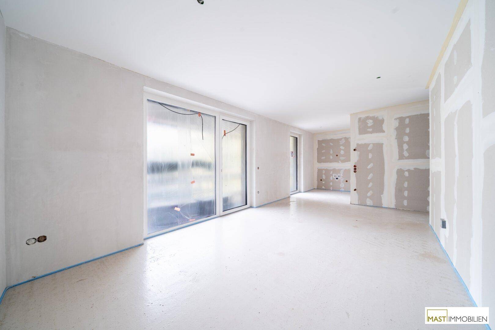 Heller Rohbau mit großen Fensterfronten und Blick in einen weiteren unfertigen Raum.