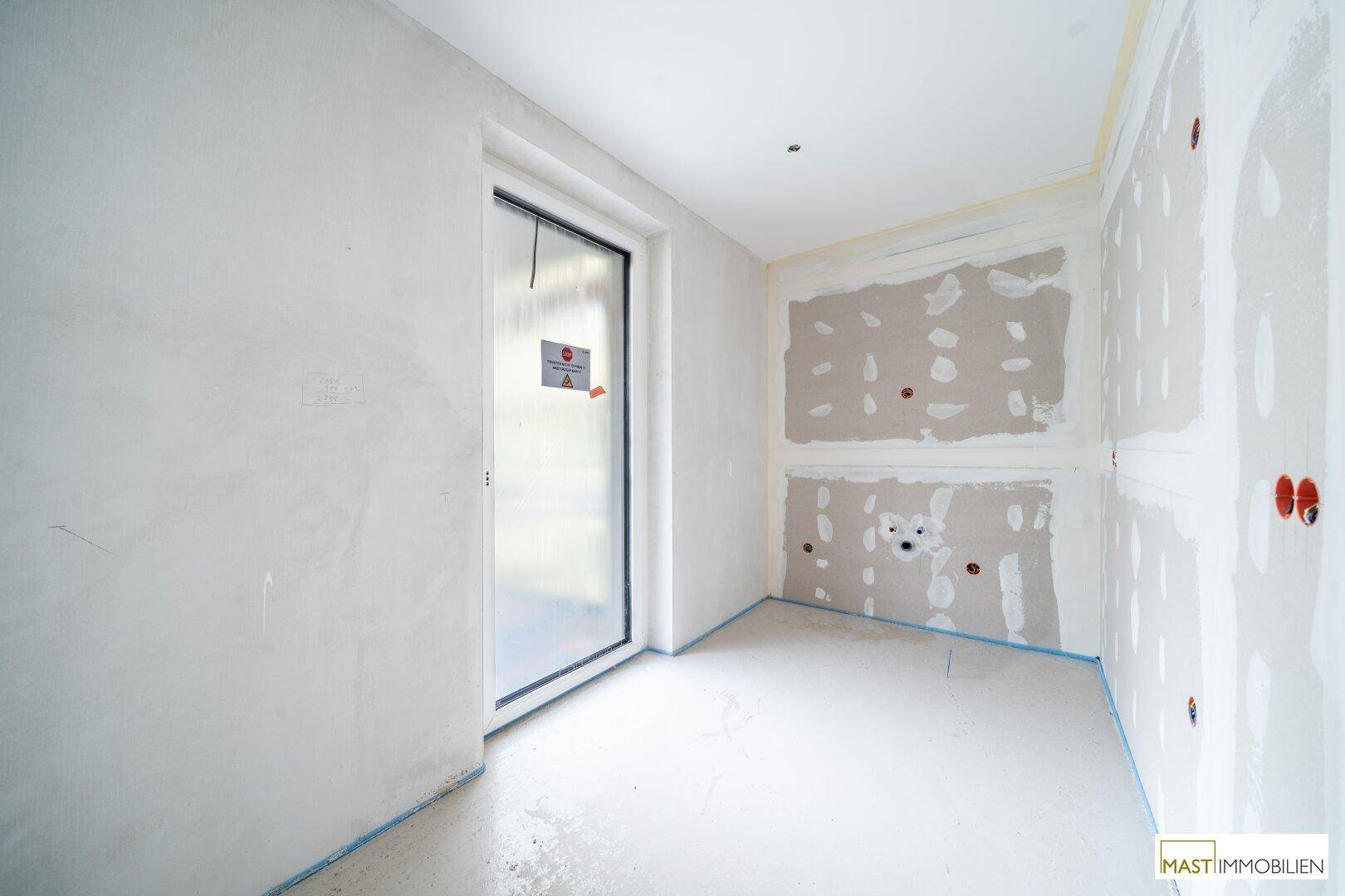 Rohbauzimmer mit Trockenbauwänden, Elektroinstallationen und einem abgedeckten Fenster.