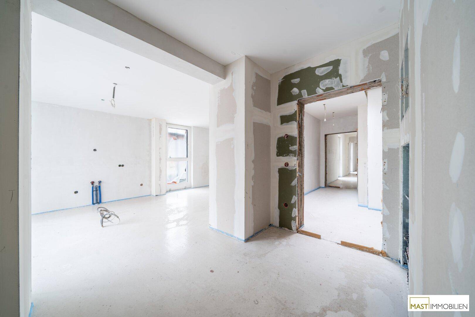 Rohbau eines hellen Raumes mit sichtbaren Installationen und unfertigen Wänden.