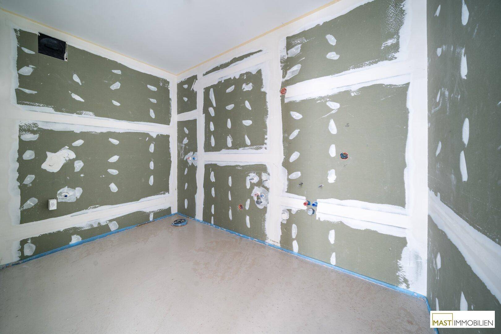 Badezimmer im Rohbau mit grünen Gipskartonplatten und sichtbaren Wasseranschlüssen.