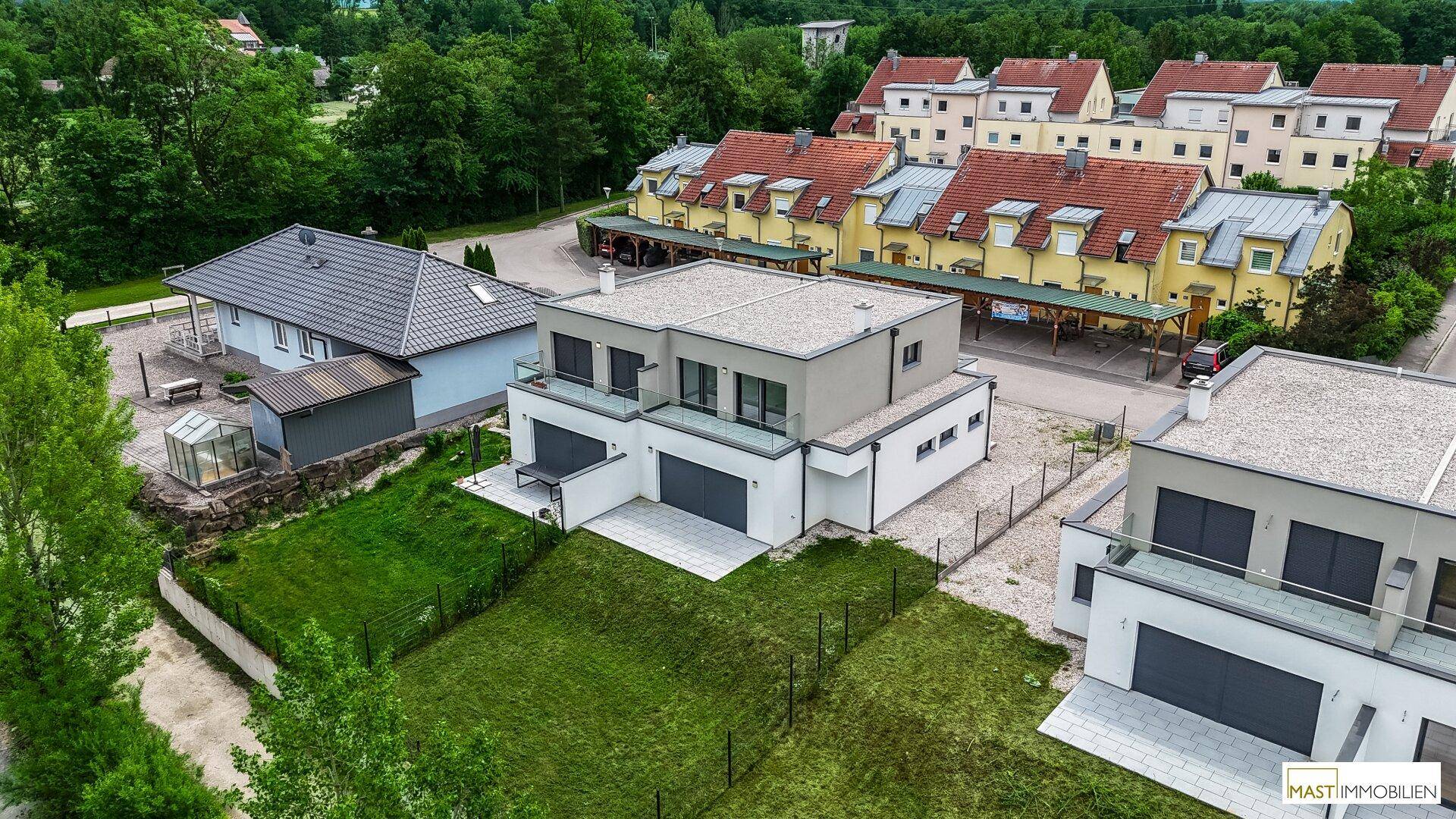 Luftaufnahme von modernen Doppelhäusern mit Gärten und angrenzender Wohnsiedlung in grüner Umgebung.