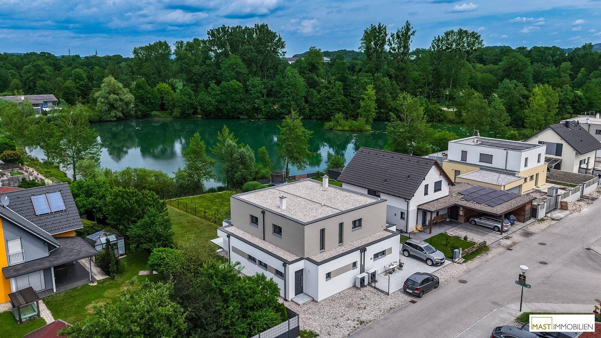 Panoramablick auf das moderne Haus, die Nachbarschaft und den idyllischen See im Hintergrund.