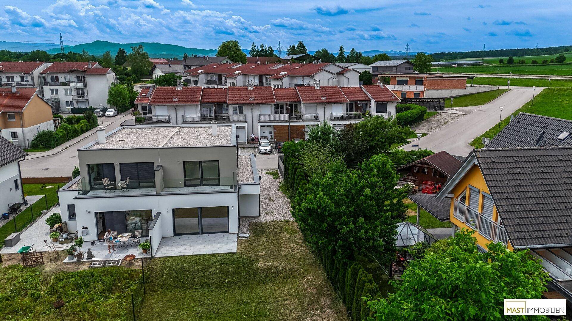 Luftaufnahme eines modernen Hauses mit Flachdach, Garten und umliegender Wohnsiedlung.