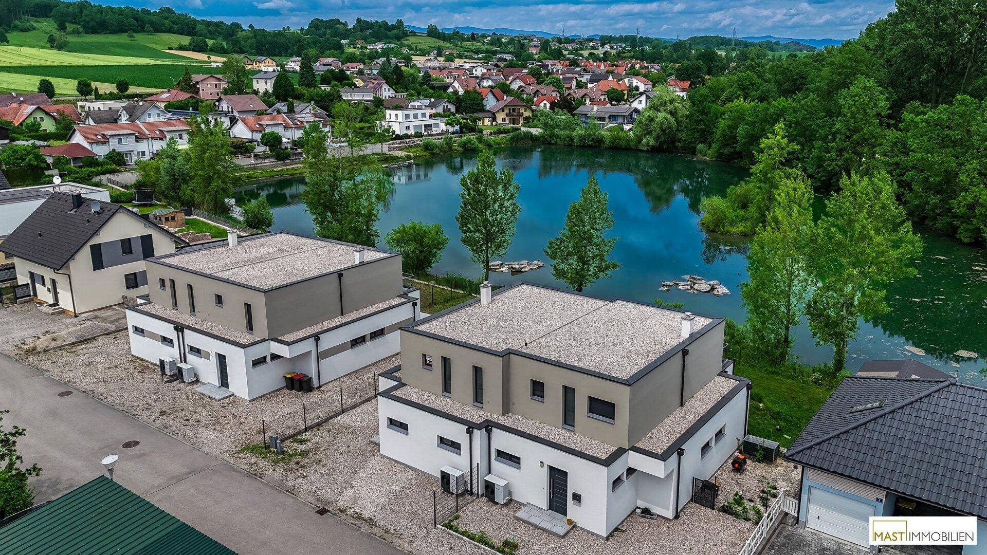 Moderne Doppelhäuser mit Flachdach und Blick auf einen malerischen See in ländlicher Umgebung.