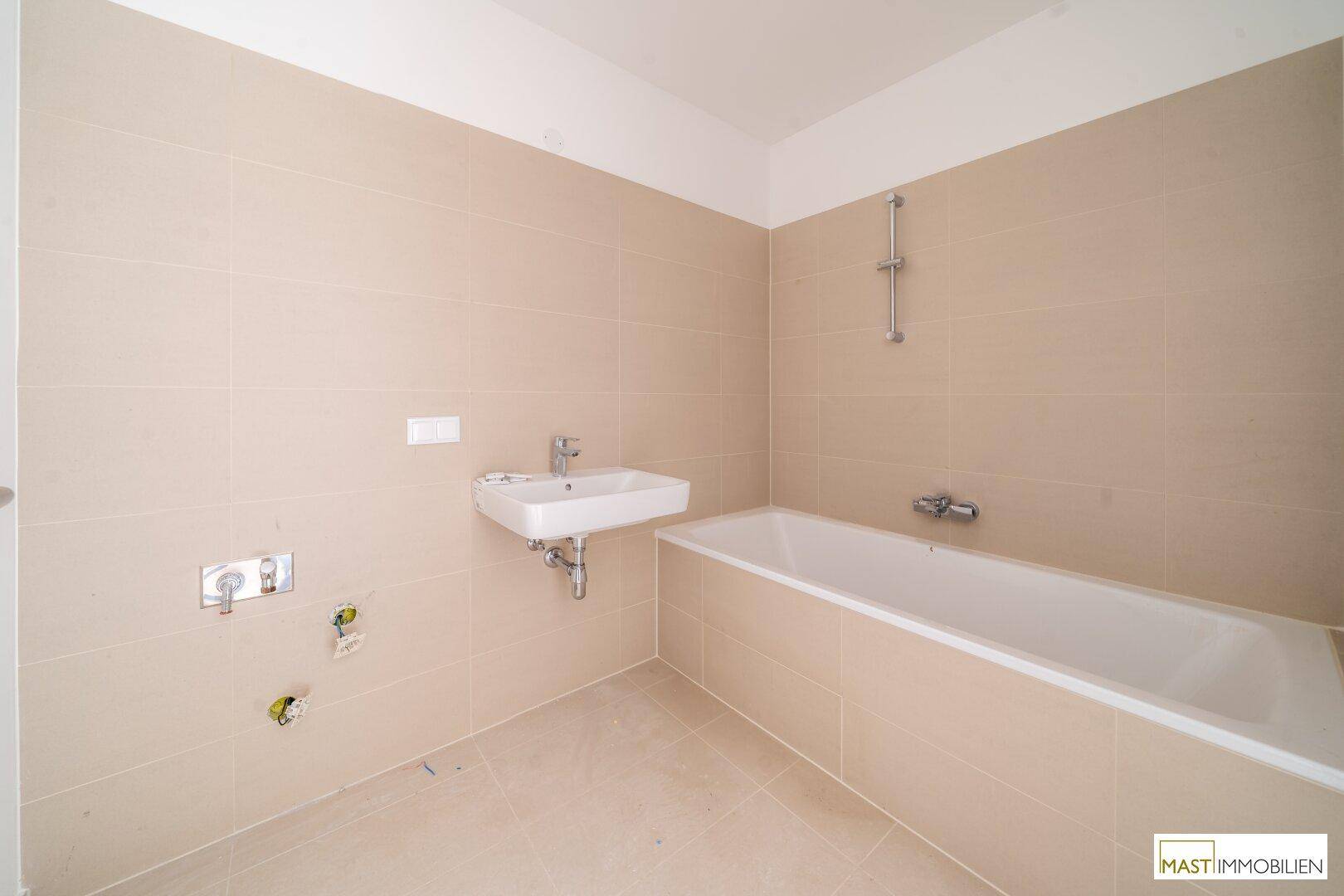 Modernes Badezimmer mit beigefarbenen Fliesen, Badewanne und Waschbecken, noch im Ausbau.