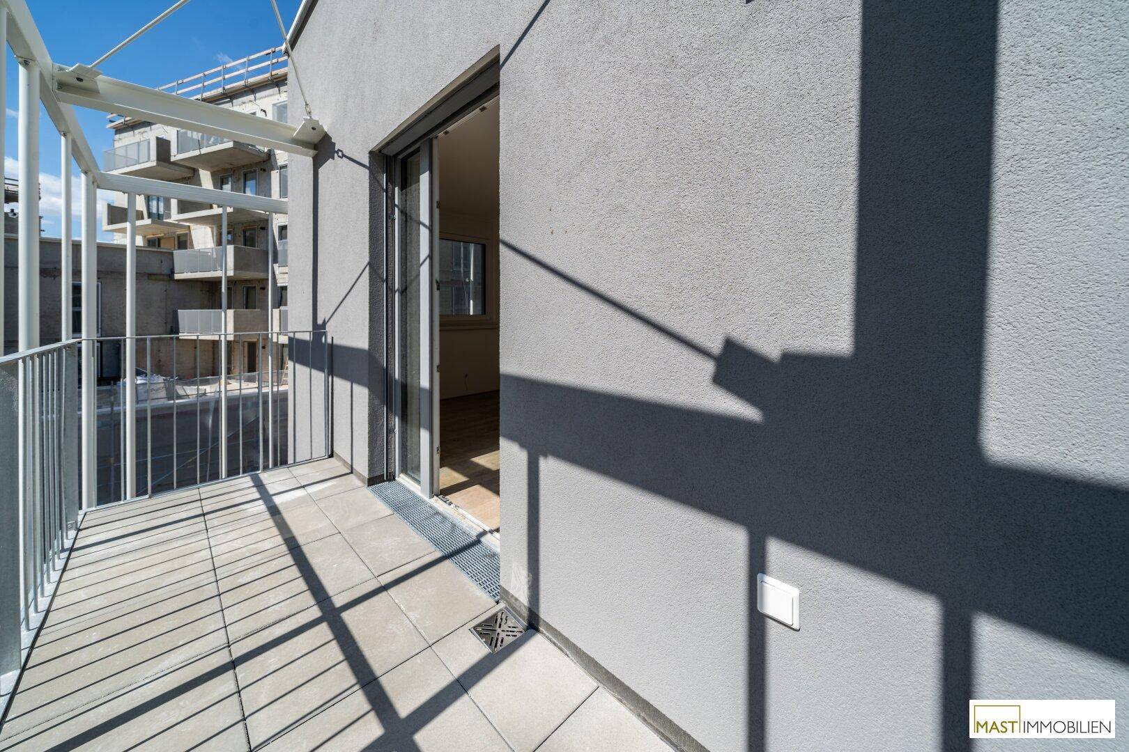 Heller Balkon mit Fliesenboden und Zugang zu einem Innenraum, umgeben von moderner Architektur.